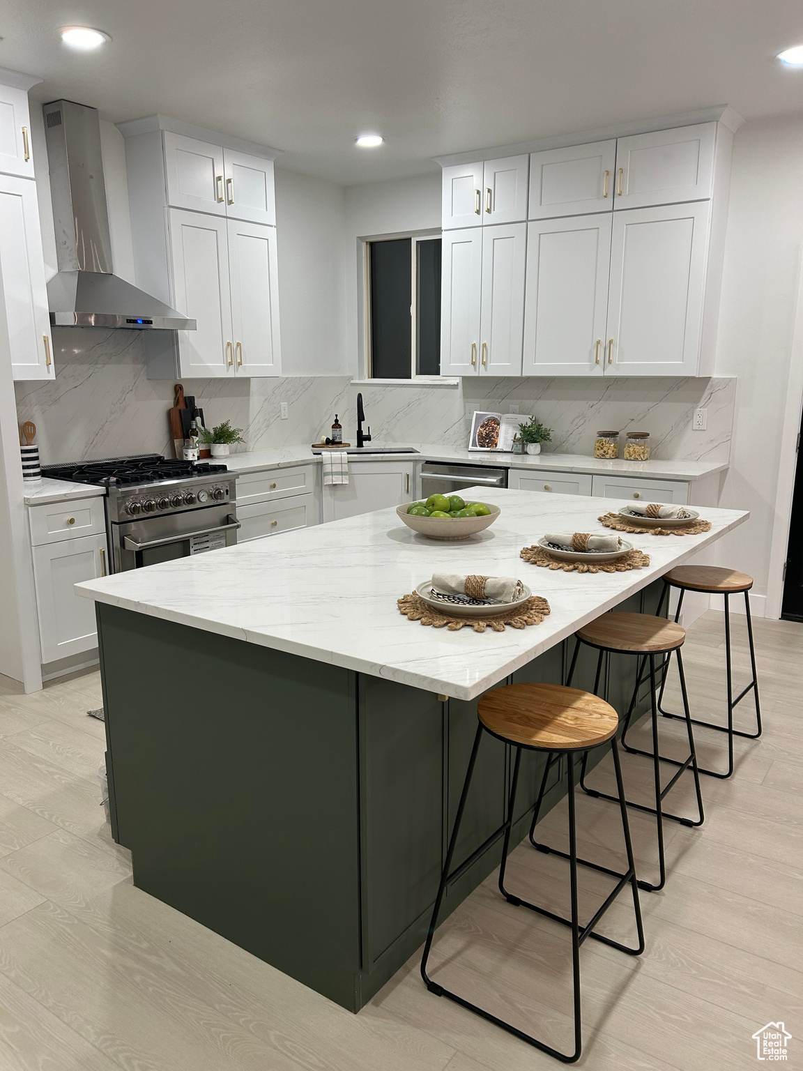 Kitchen featuring high end stove, a center island, white cabinets, and wall chimney range hood