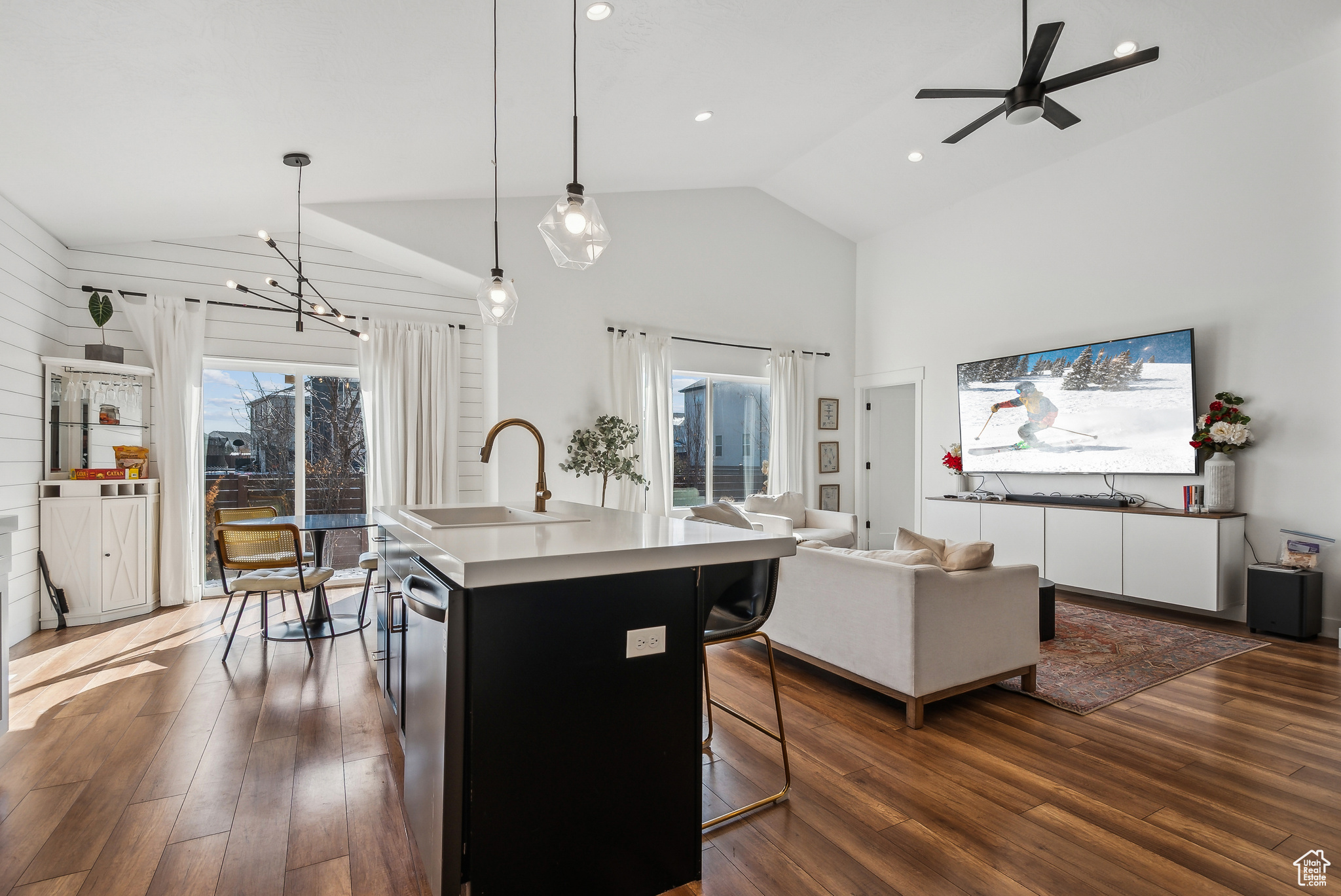 Kitchen with dark wood-type flooring, a breakfast bar area, a center island with sink, decorative light fixtures, and stainless steel dishwasher