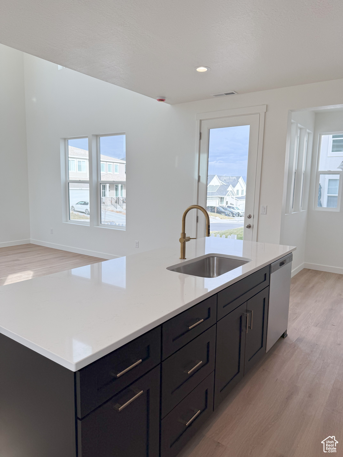 Kitchen featuring dishwasher, light hardwood / wood-style floors, a center island with sink, and sink