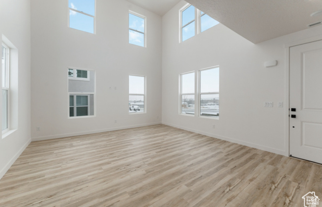 Unfurnished living room featuring a healthy amount of sunlight, a high ceiling, and light wood-type flooring