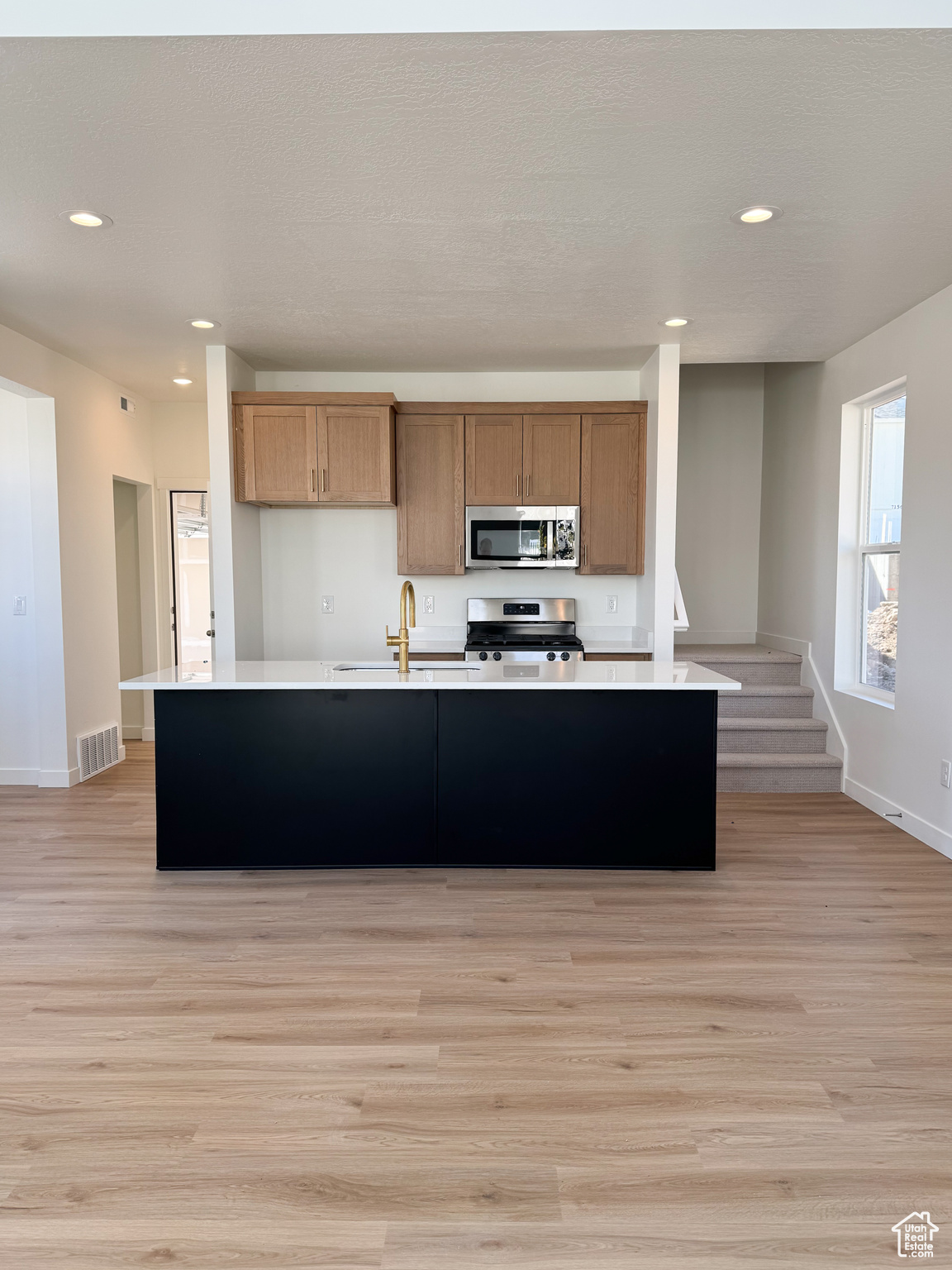 Kitchen with sink, an island with sink, light wood-type flooring, and appliances with stainless steel finishes