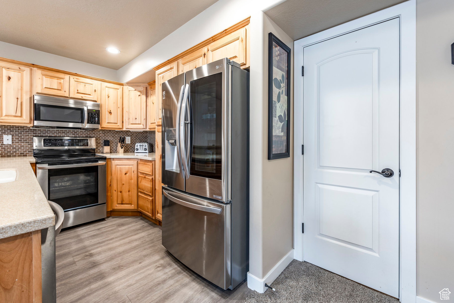 Kitchen featuring backsplash, light brown cabinets, stainless steel appliances, and light wood-type flooring