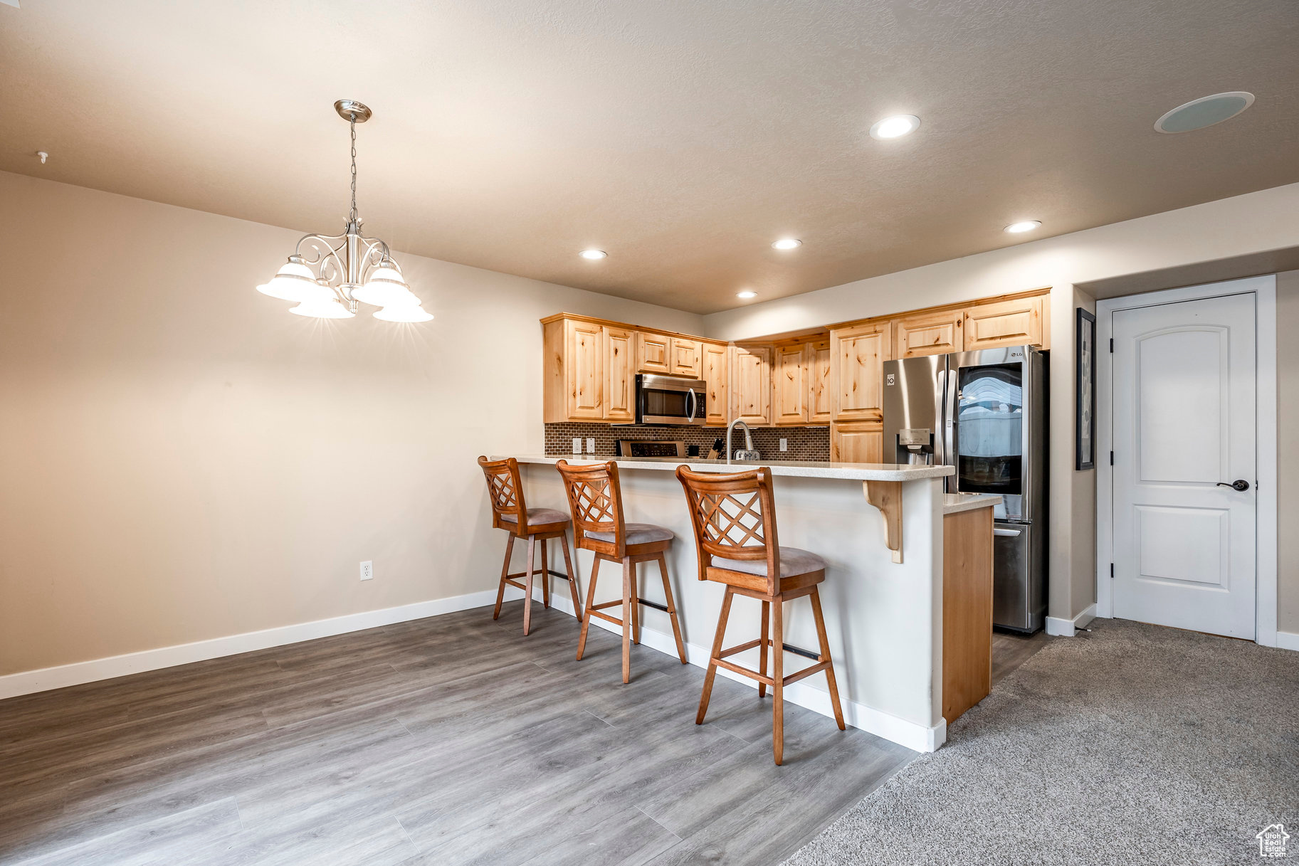 Kitchen with an inviting chandelier, light hardwood / wood-style floors, pendant lighting, a breakfast bar area, and appliances with stainless steel finishes