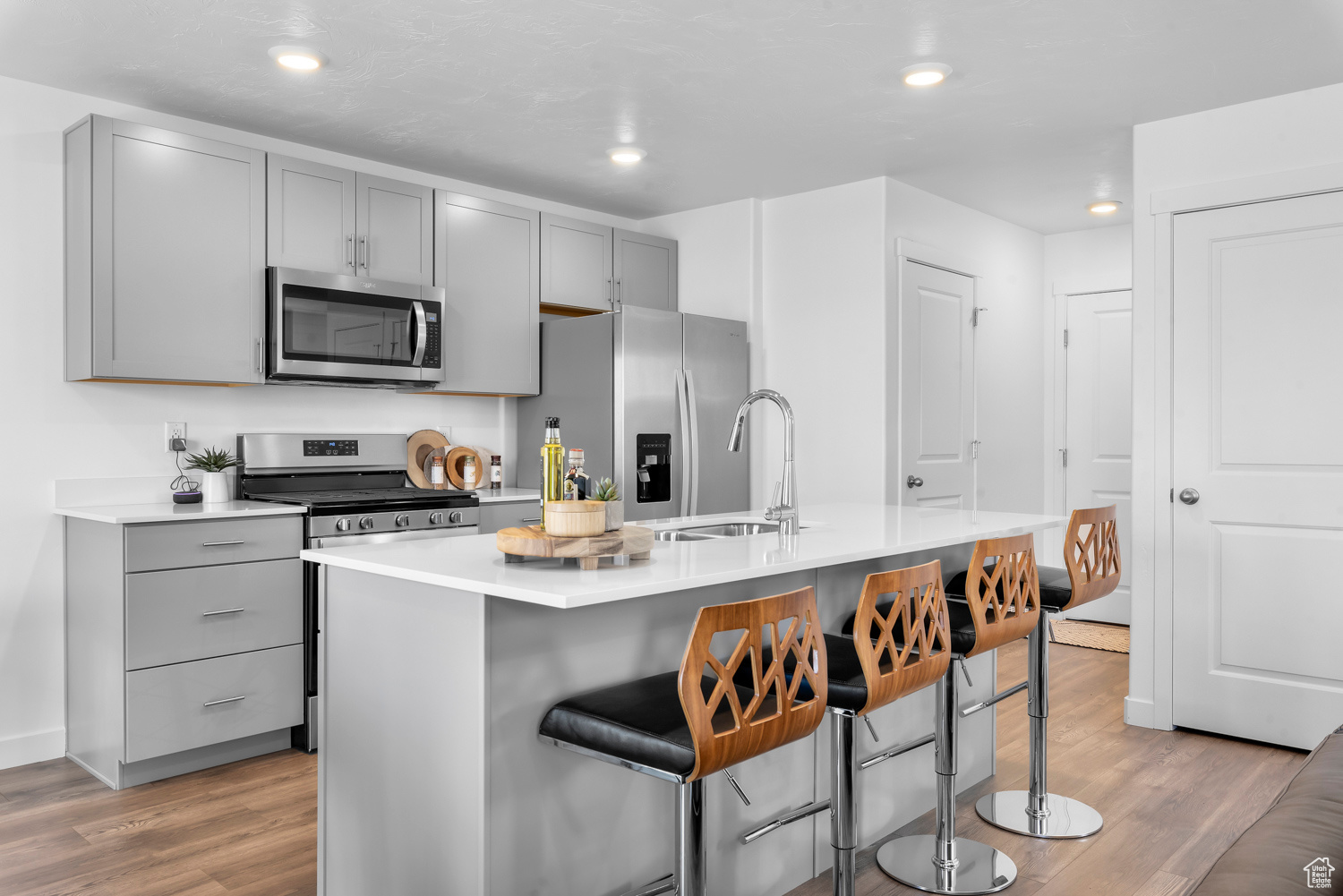 Kitchen with sink, light hardwood / wood-style flooring, an island with sink, gray cabinets, and appliances with stainless steel finishes