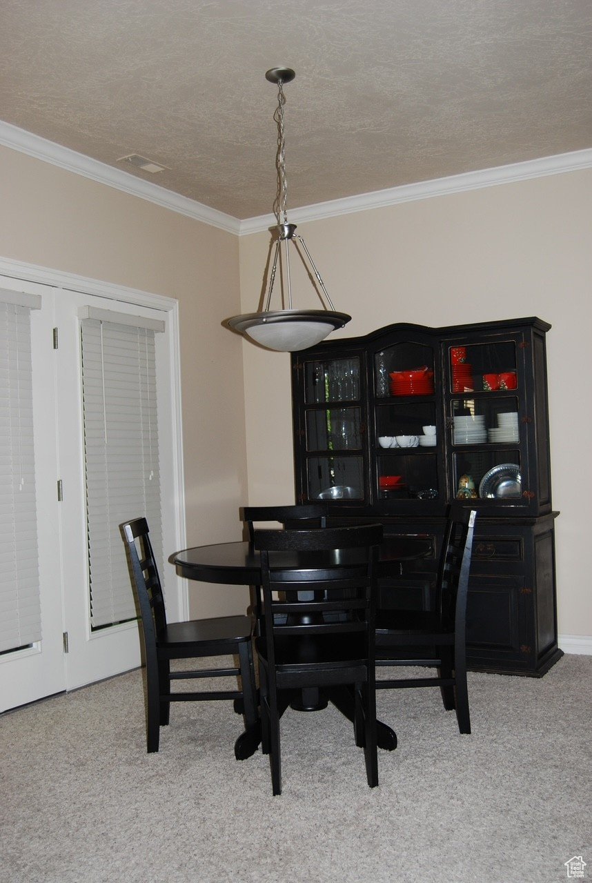 Dining area featuring light carpet, a textured ceiling, and ornamental molding