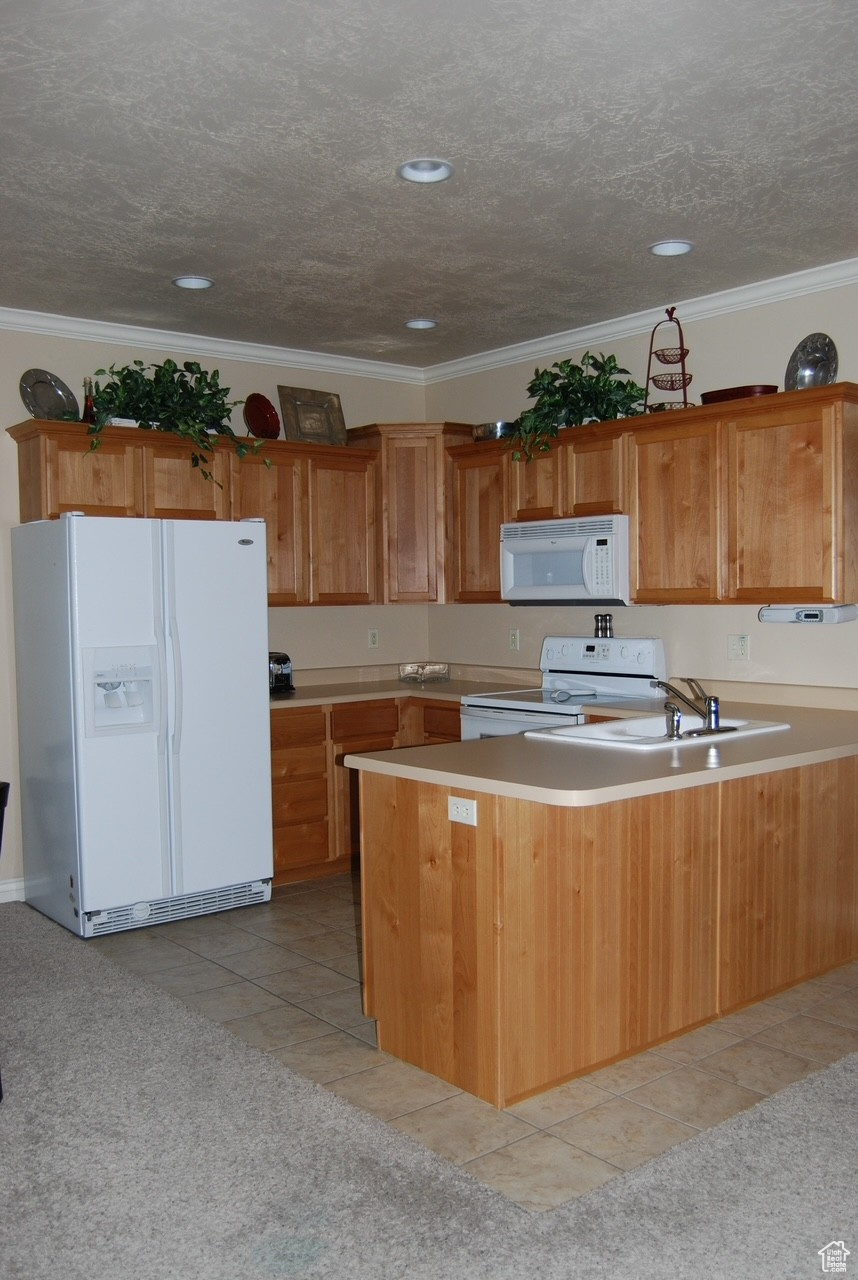 Kitchen featuring kitchen peninsula, ornamental molding, a textured ceiling, white appliances, and light colored carpet