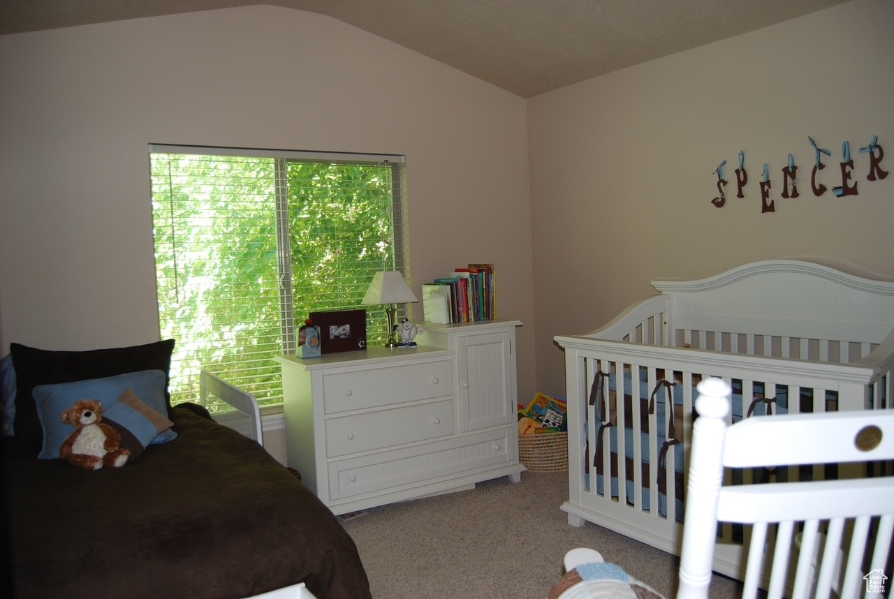 Bedroom featuring light colored carpet, a nursery area, and lofted ceiling