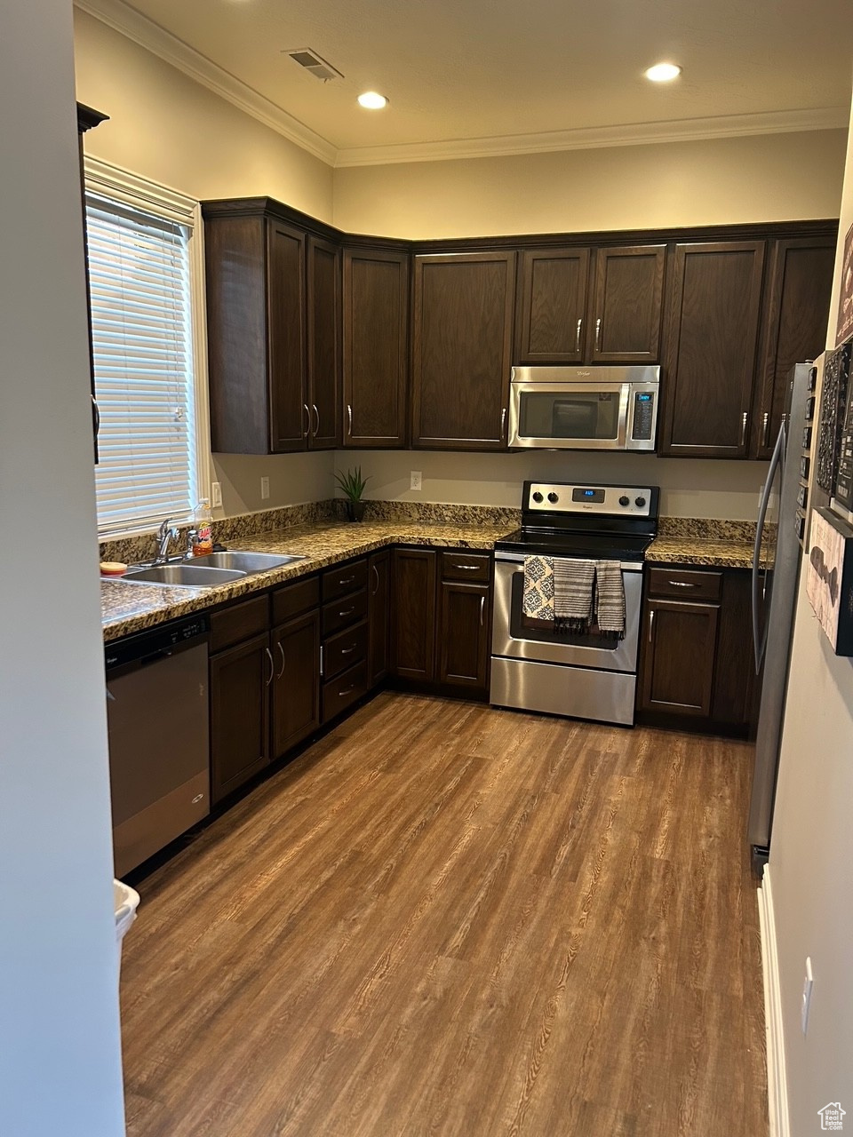 Kitchen featuring appliances with stainless steel finishes, dark hardwood / wood-style flooring, ornamental molding, dark brown cabinets, and sink