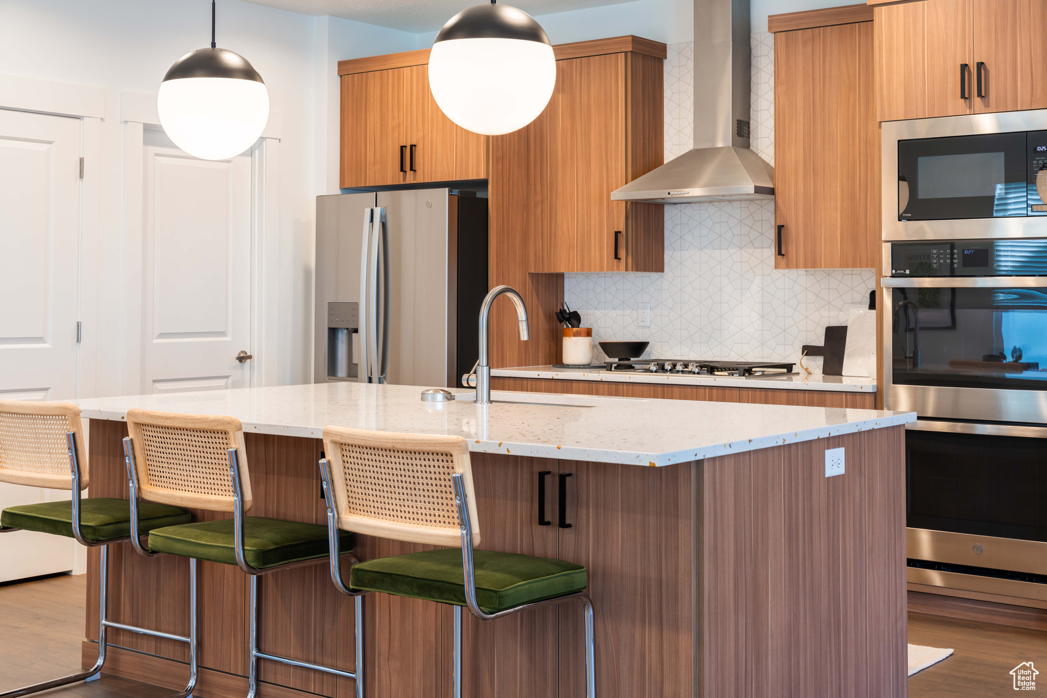 Kitchen featuring sink, wall chimney range hood, wood-type flooring, a center island with sink, and appliances with stainless steel finishes