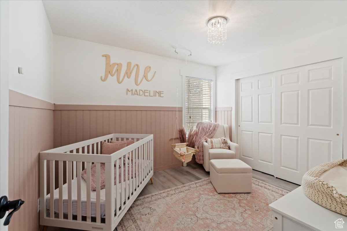 Bedroom featuring a notable chandelier, light hardwood / wood-style floors, a crib, and a closet