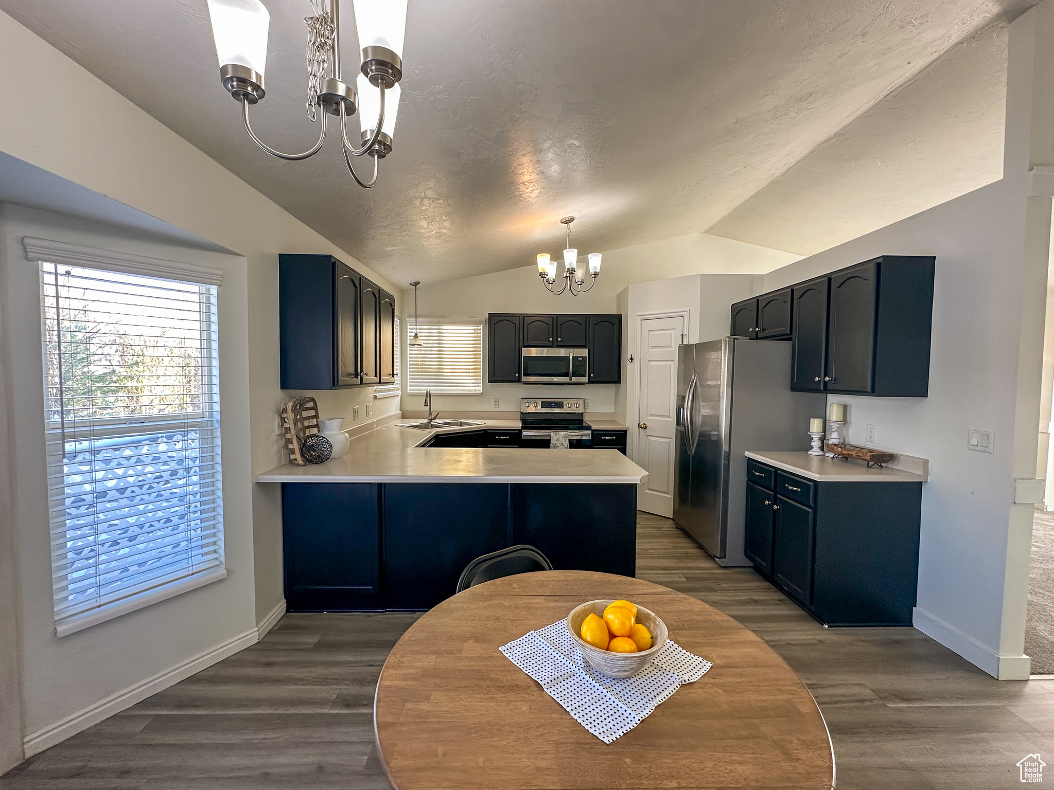 Kitchen with lofted ceiling, hanging light fixtures, appliances with stainless steel finishes, a notable chandelier, and kitchen peninsula