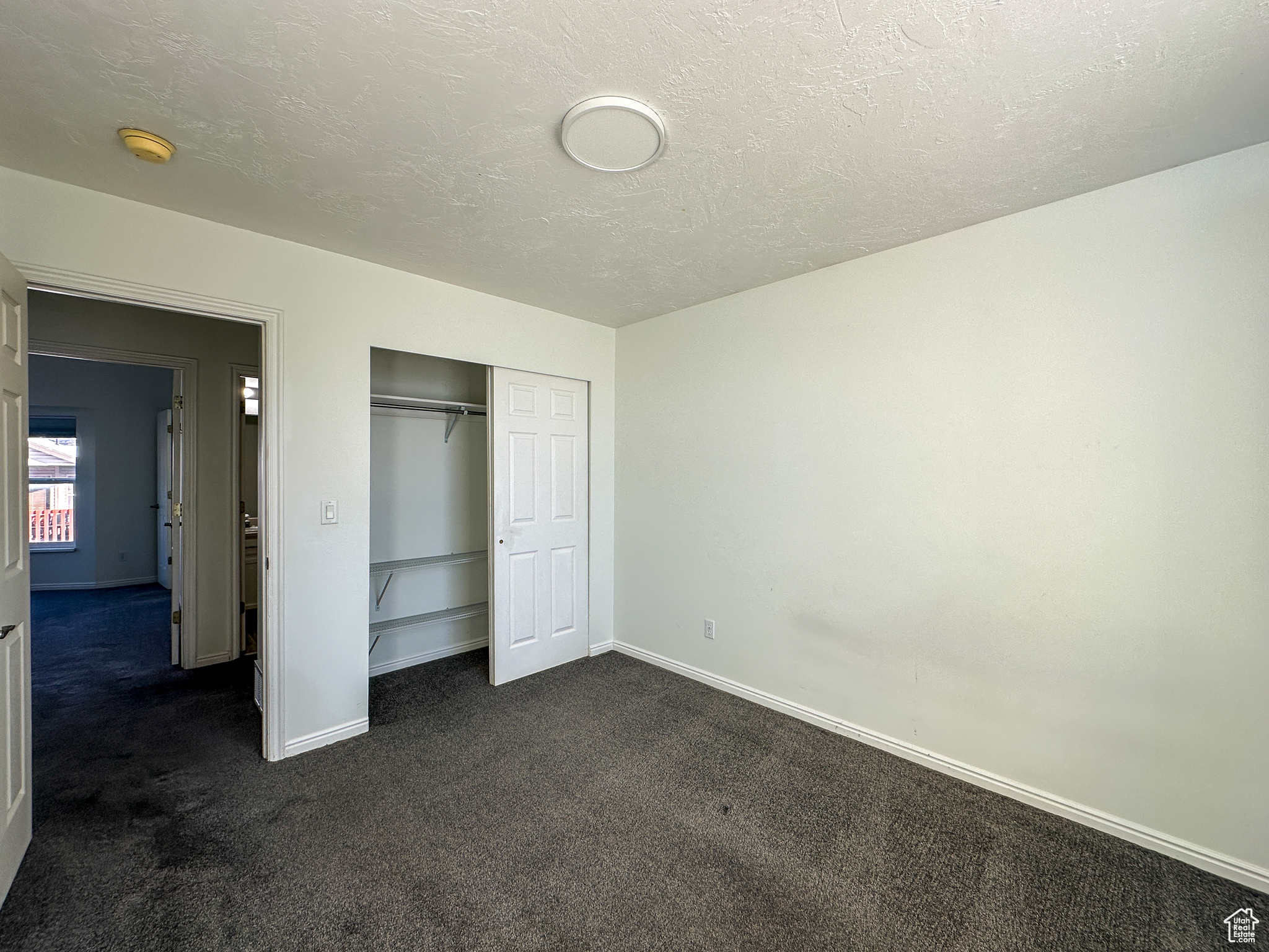 Unfurnished bedroom with dark carpet, a textured ceiling, and a closet