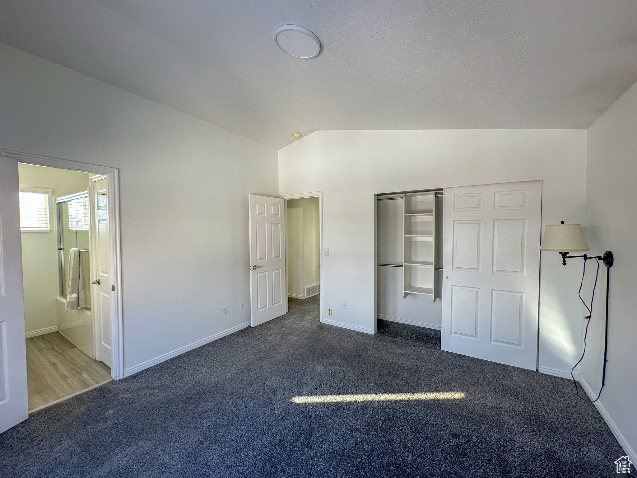 Unfurnished bedroom featuring ensuite bath, a closet, lofted ceiling, and dark colored carpet