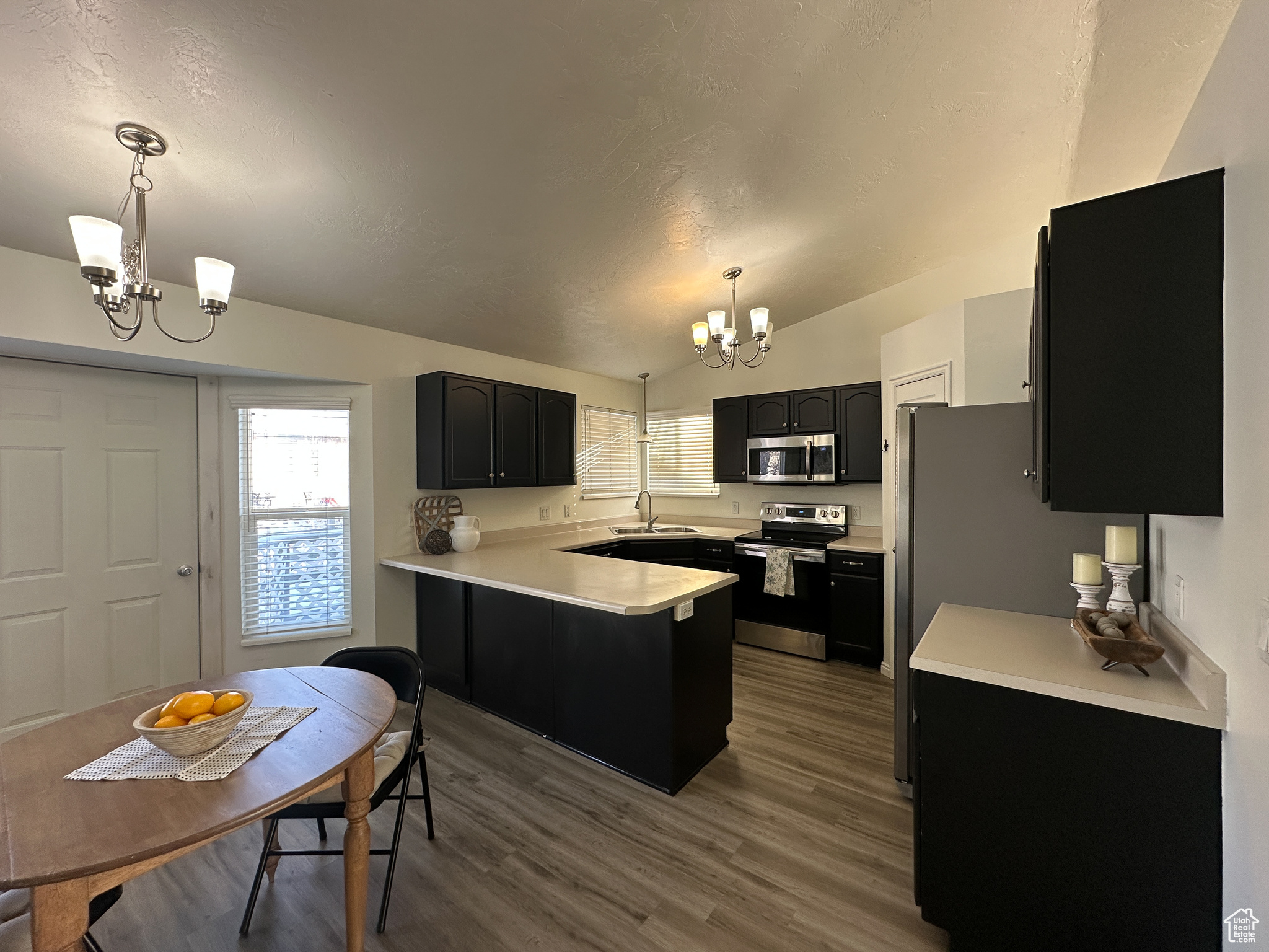 Kitchen with vaulted ceiling, hanging light fixtures, appliances with stainless steel finishes, and an inviting chandelier