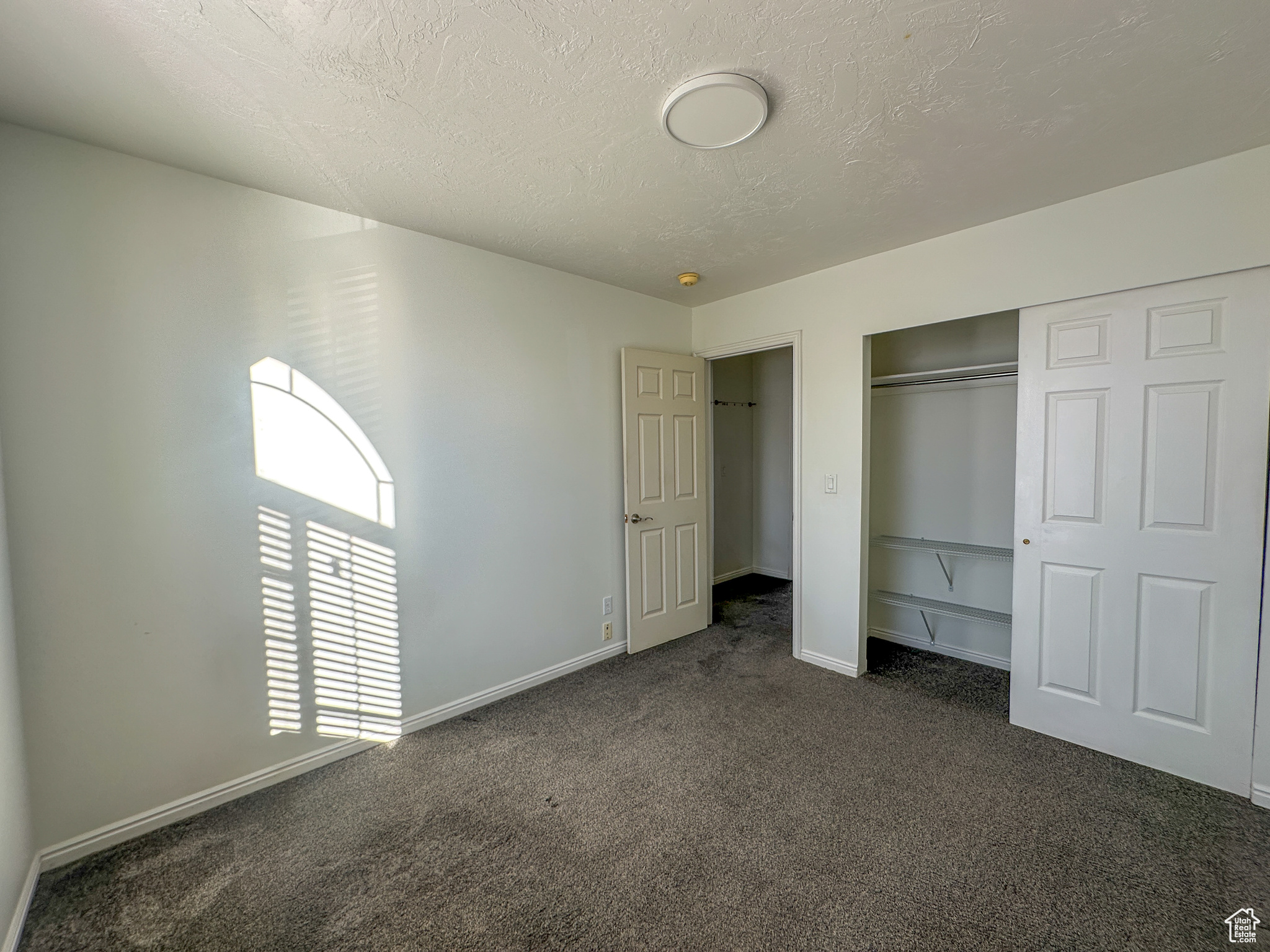 Unfurnished bedroom with dark colored carpet, a textured ceiling, and a closet