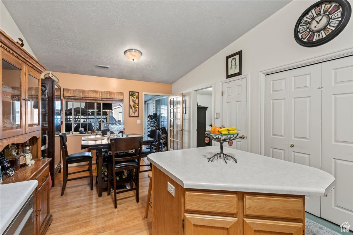 Kitchen featuring lofted ceiling, a kitchen island, light wood-type flooring, and a textured ceiling