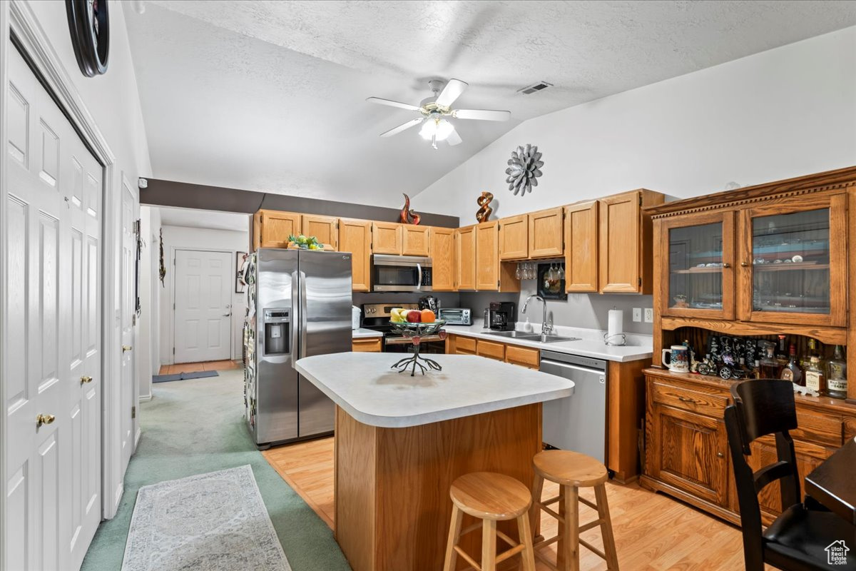 Kitchen with appliances with stainless steel finishes, a breakfast bar, sink, a center island, and lofted ceiling