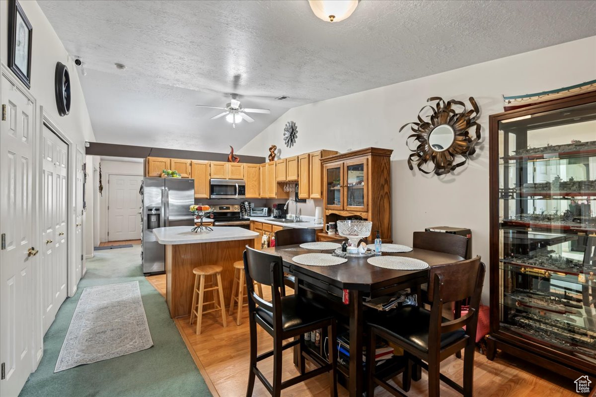 Dining room featuring a textured ceiling, light hardwood / wood-style flooring, sink, and vaulted ceiling