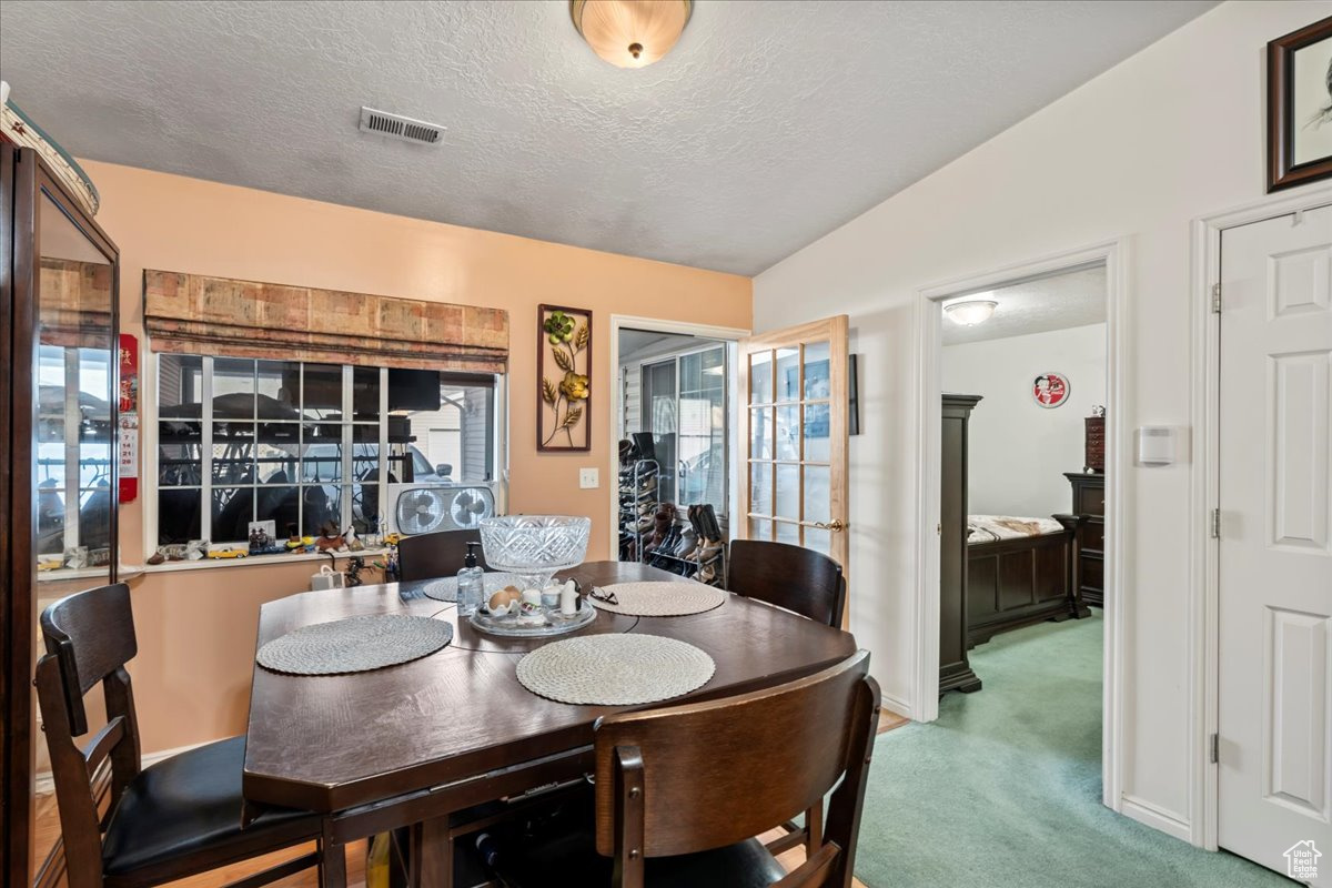 Dining area with a textured ceiling, carpet, and lofted ceiling