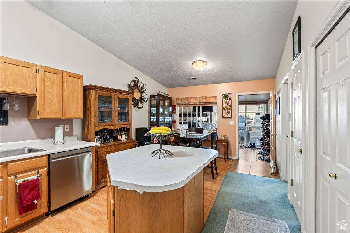 Kitchen with light hardwood / wood-style flooring, stainless steel dishwasher, a textured ceiling, vaulted ceiling, and a kitchen island