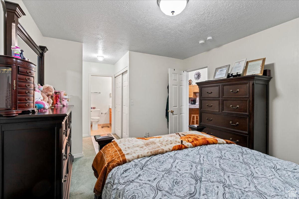 Carpeted bedroom featuring a textured ceiling and ensuite bath