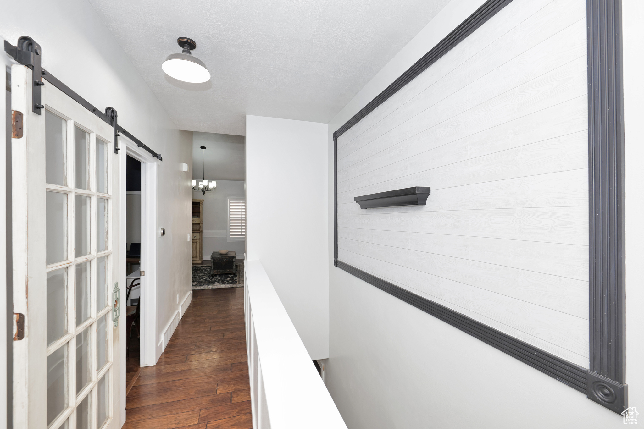 Hall with a barn door, dark wood-type flooring, and a notable chandelier