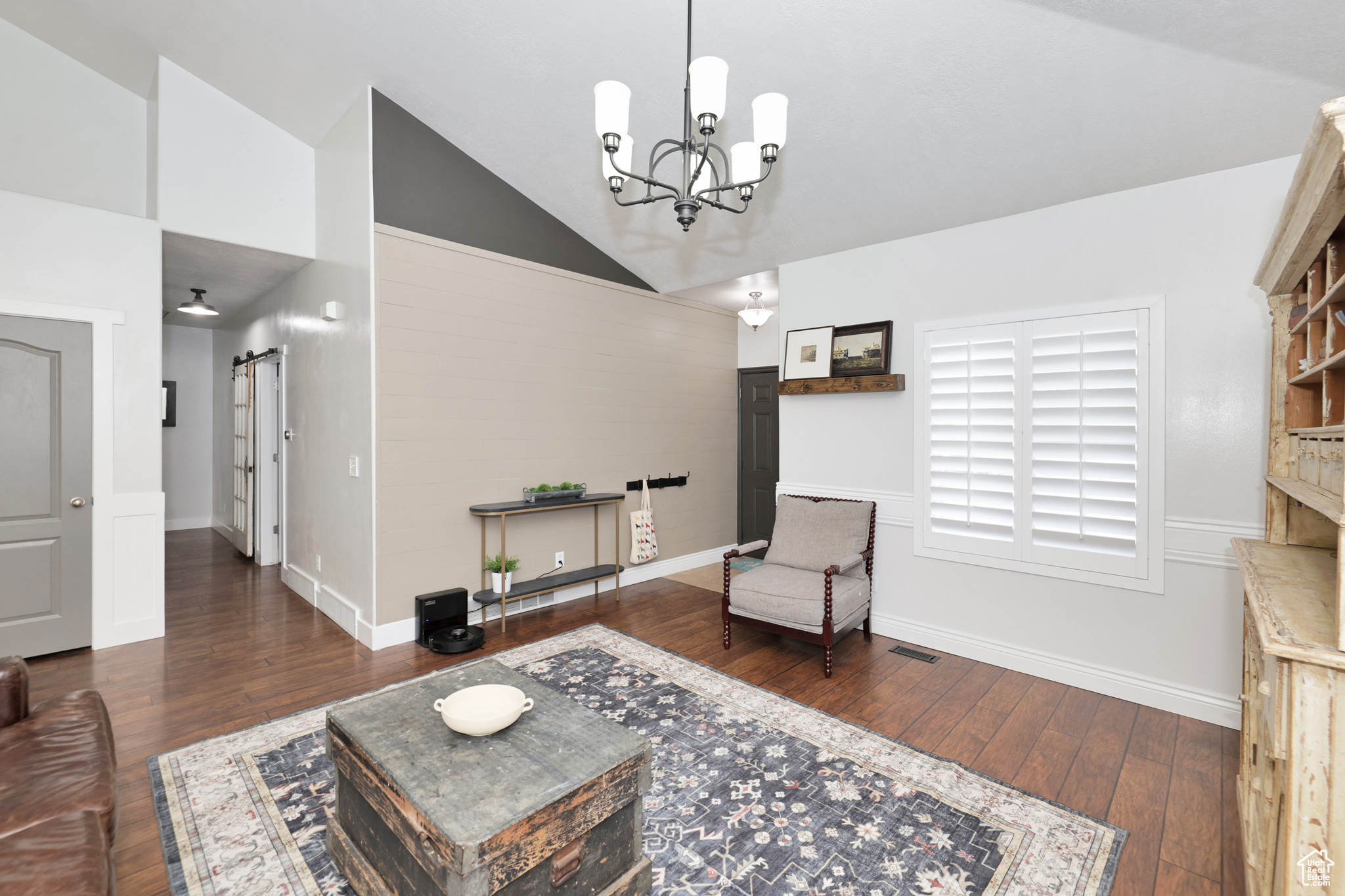 Living area featuring a barn door, dark hardwood / wood-style flooring, high vaulted ceiling, and a chandelier