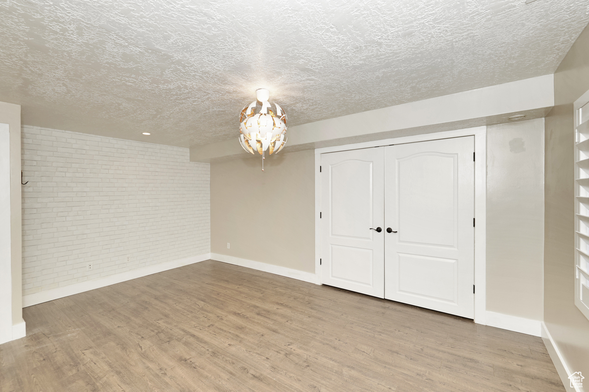 Unfurnished bedroom featuring a closet, a textured ceiling, brick wall, and light hardwood / wood-style flooring