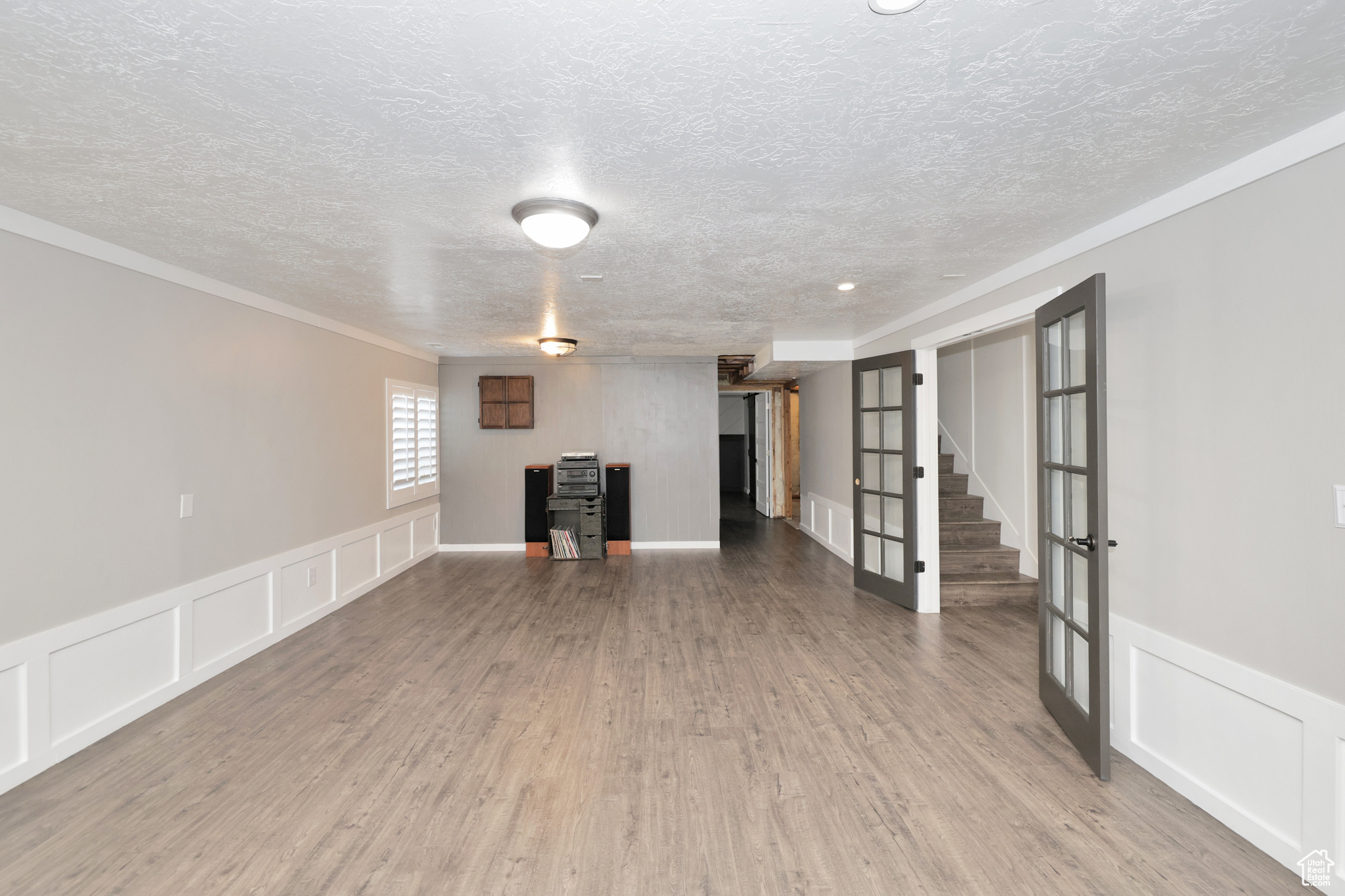 Basement with french doors, light wood-type flooring, and a textured ceiling