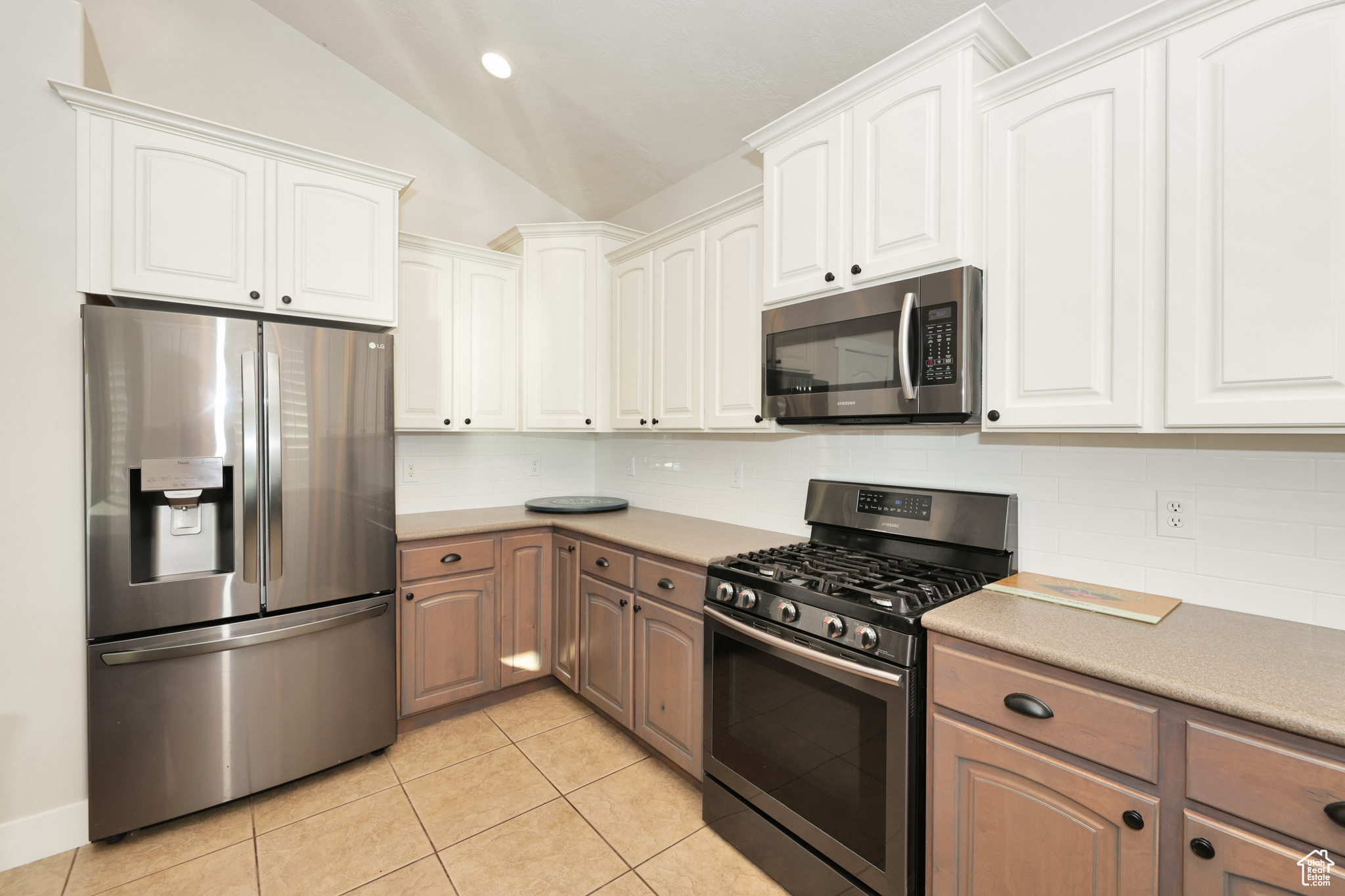 Kitchen with white cabinetry, lofted ceiling, appliances with stainless steel finishes, and tasteful backsplash