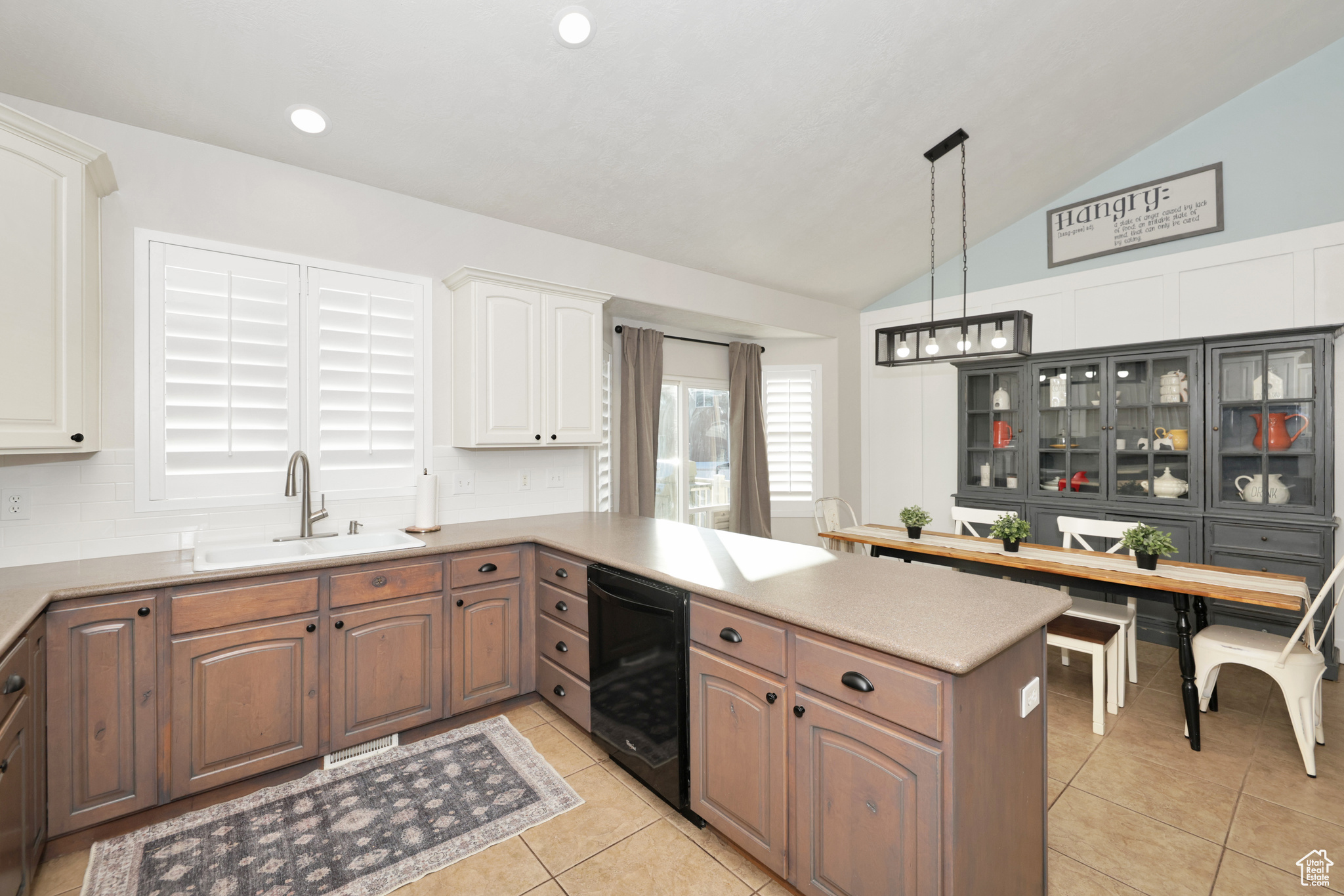 Kitchen with sink, kitchen peninsula, pendant lighting, vaulted ceiling, and white cabinets