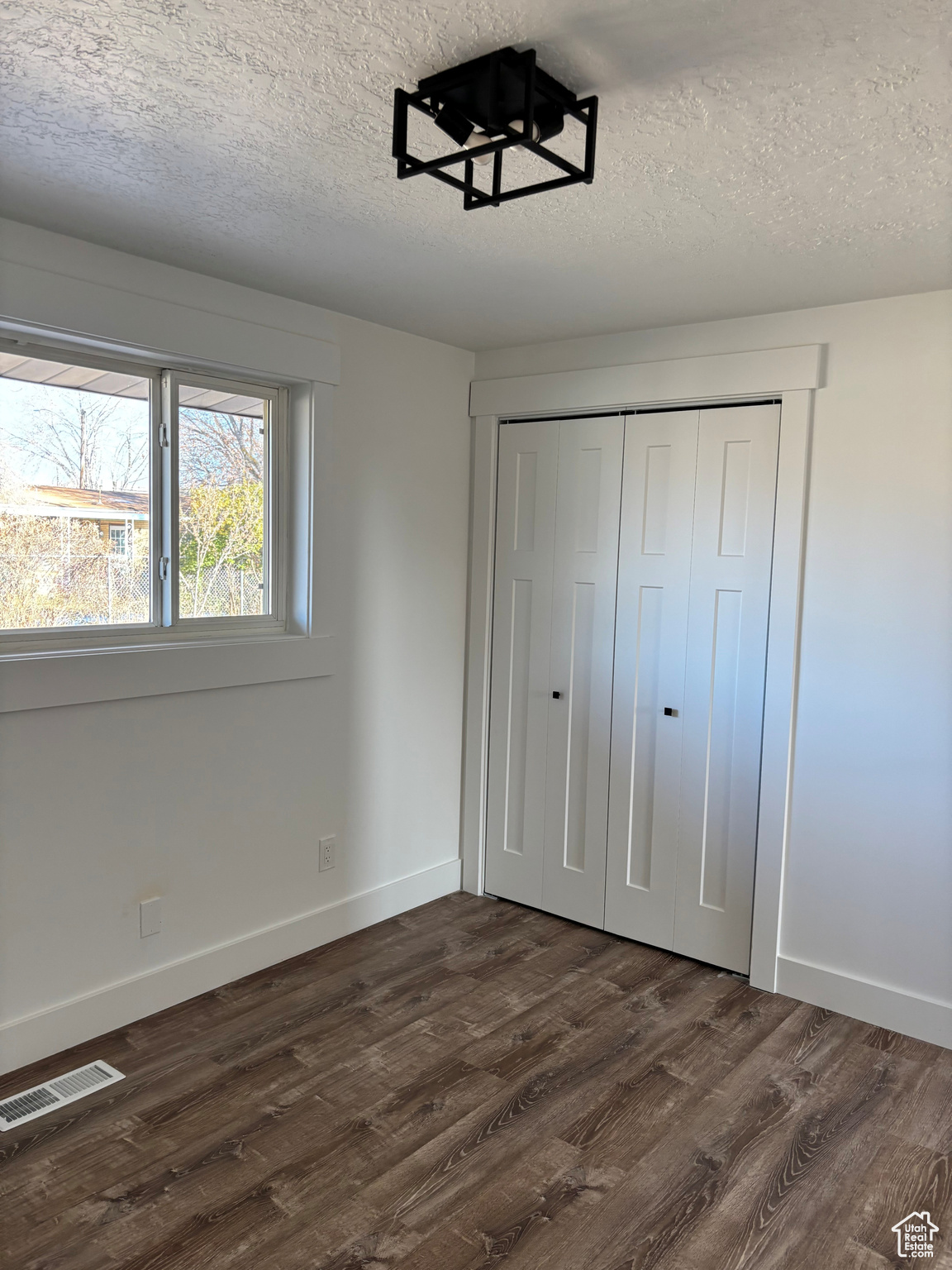 Unfurnished bedroom with a textured ceiling, dark hardwood / wood-style flooring, and a closet