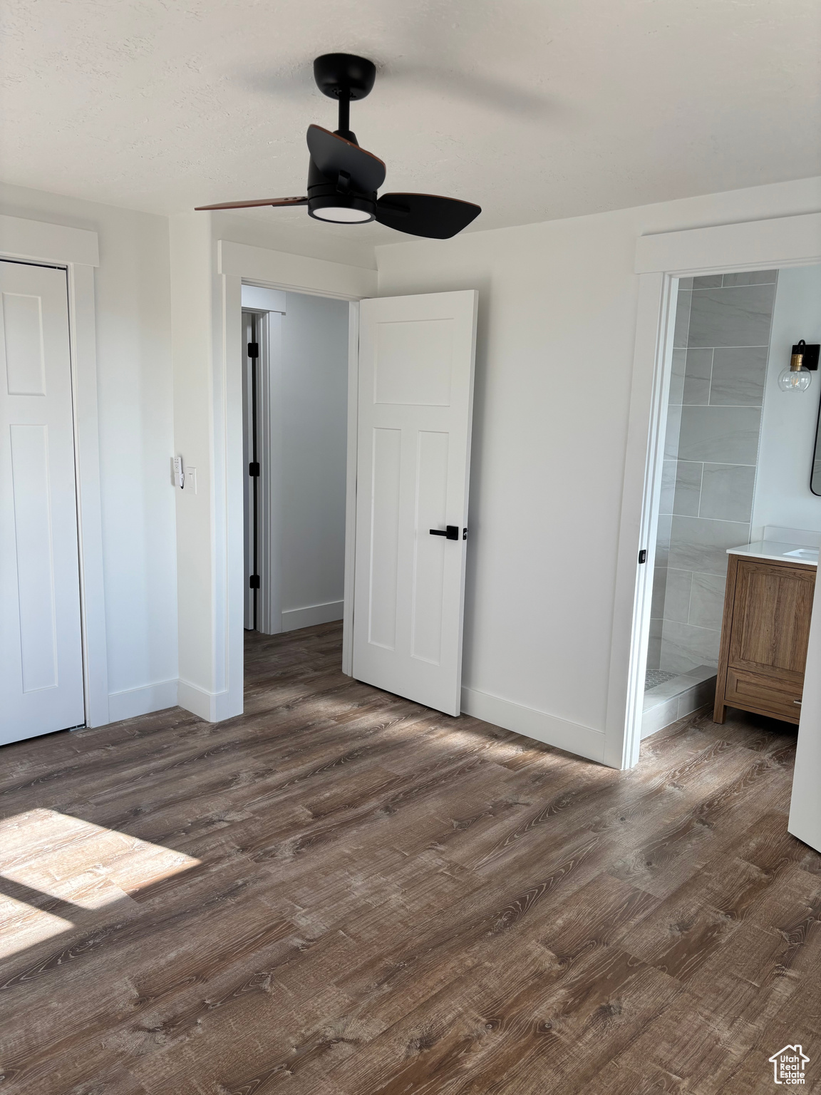 Unfurnished bedroom with ensuite bath, ceiling fan, and dark wood-type flooring