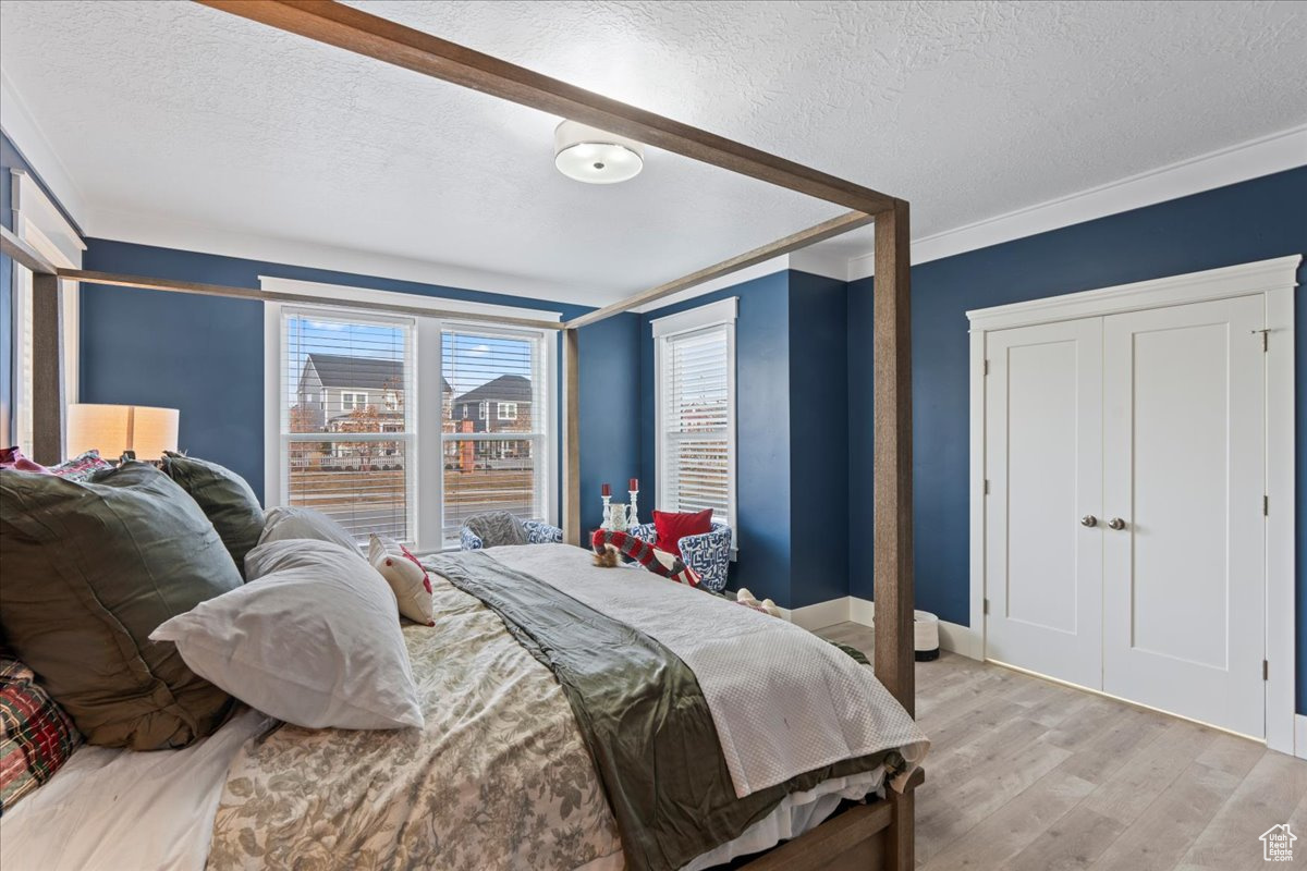 Bedroom with a textured ceiling, light wood-type flooring, and ornamental molding