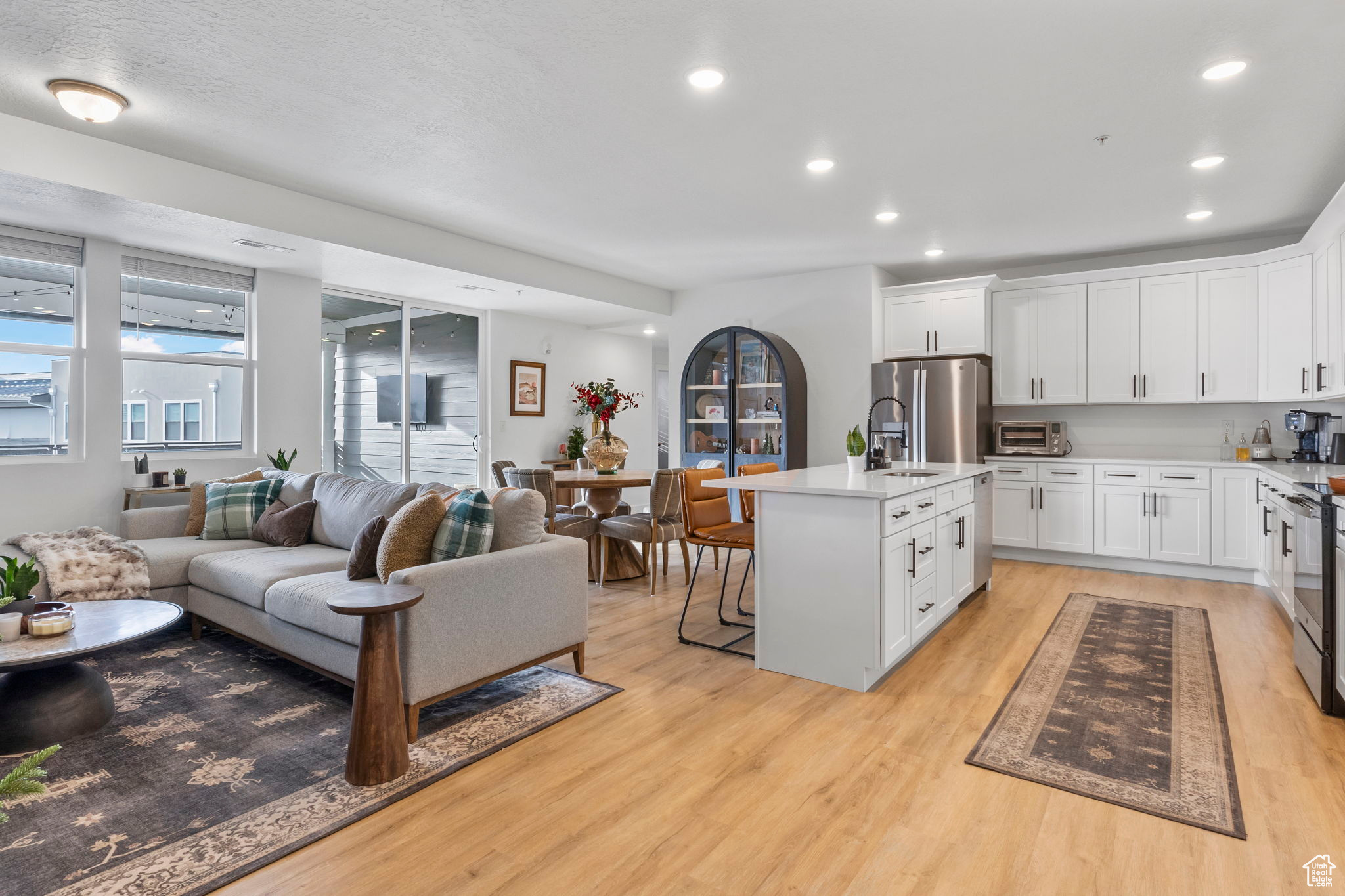 Kitchen with a kitchen breakfast bar, light wood-type flooring, appliances with stainless steel finishes, a kitchen island with sink, and white cabinets