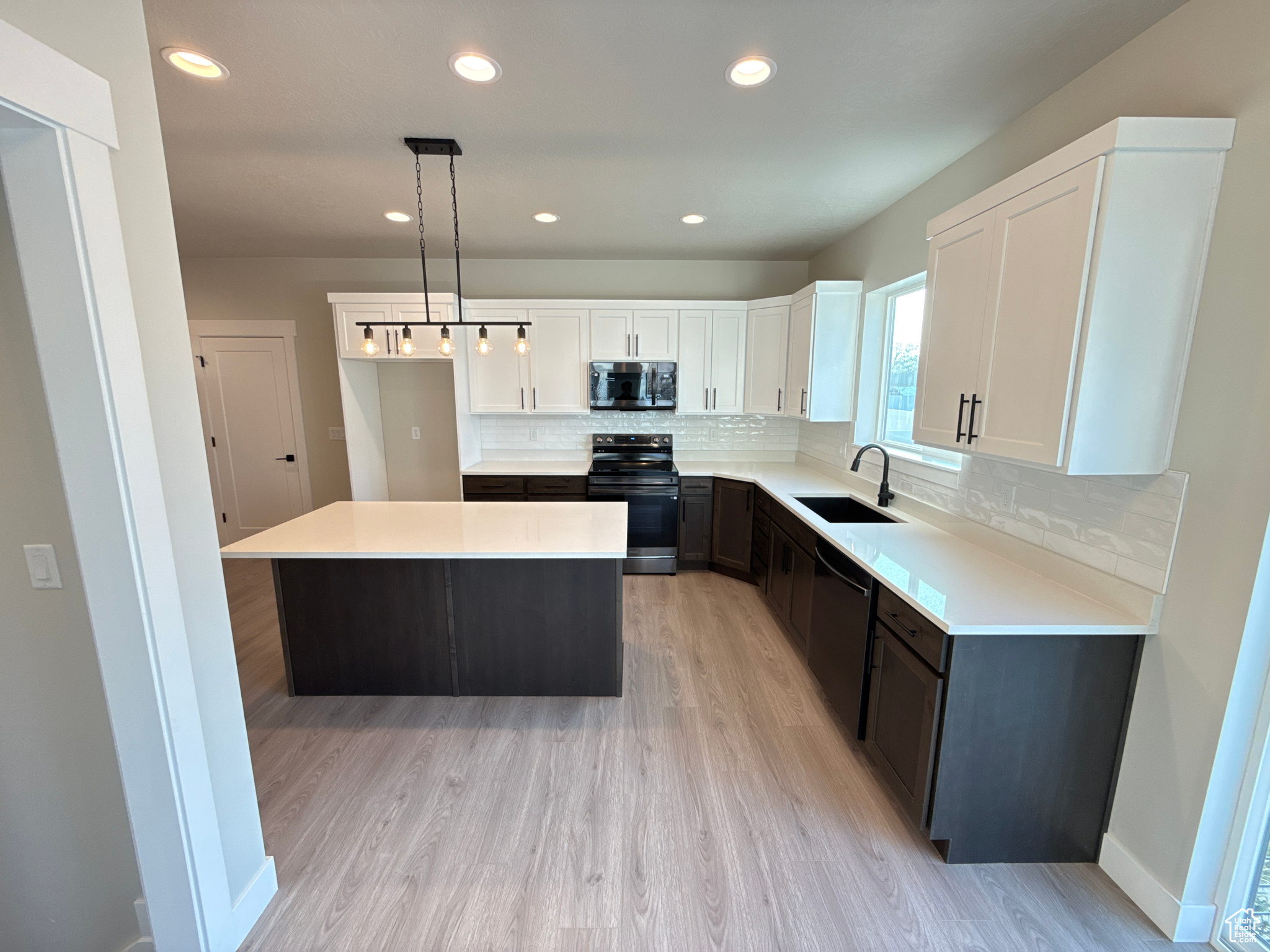 Kitchen with sink, a kitchen island, decorative light fixtures, white upper and dark lower cabinets, and appliances with black stainless steel finishes