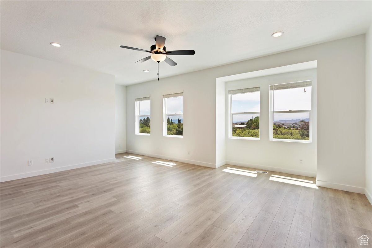 Empty room featuring ceiling fan, a textured ceiling, and light hardwood / wood-style flooring