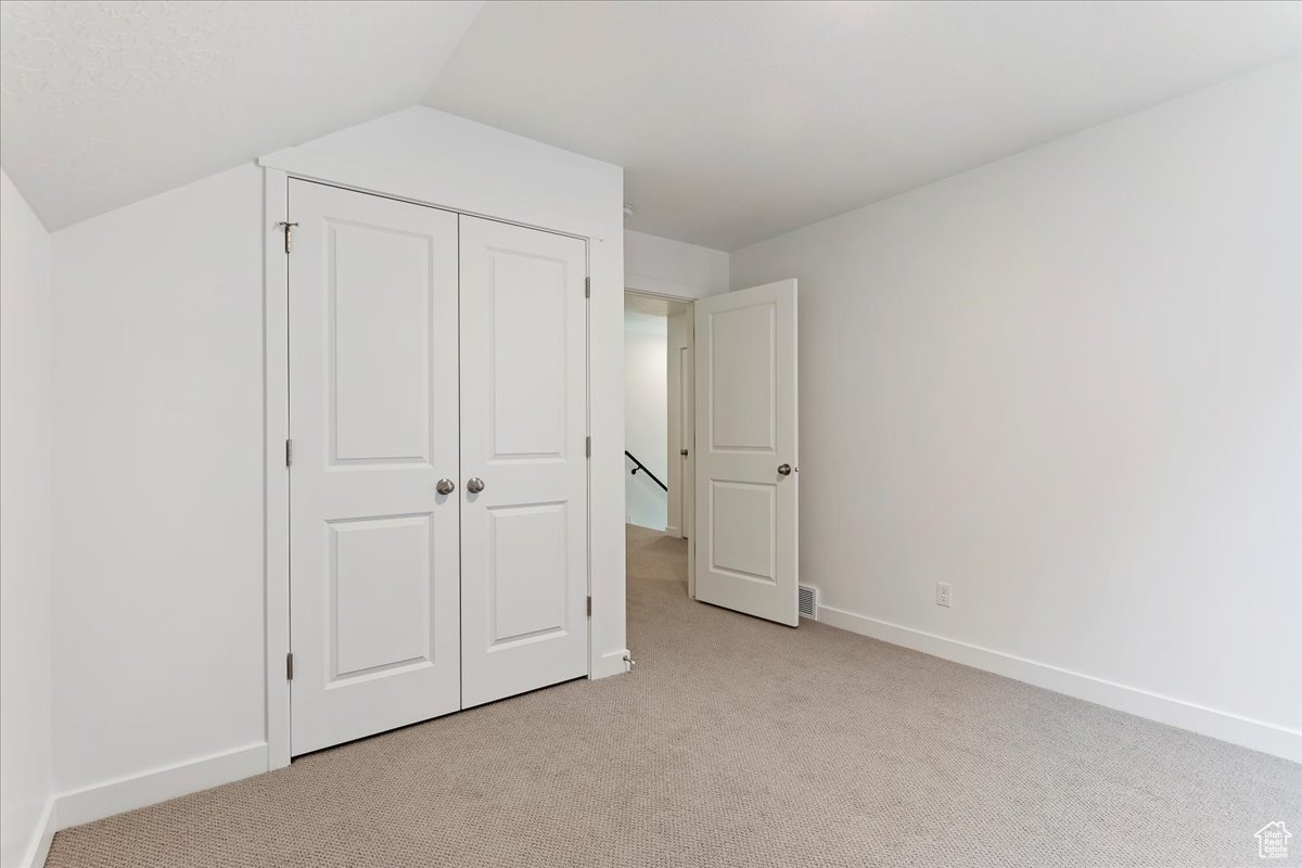 Unfurnished bedroom featuring light colored carpet, lofted ceiling, and a closet