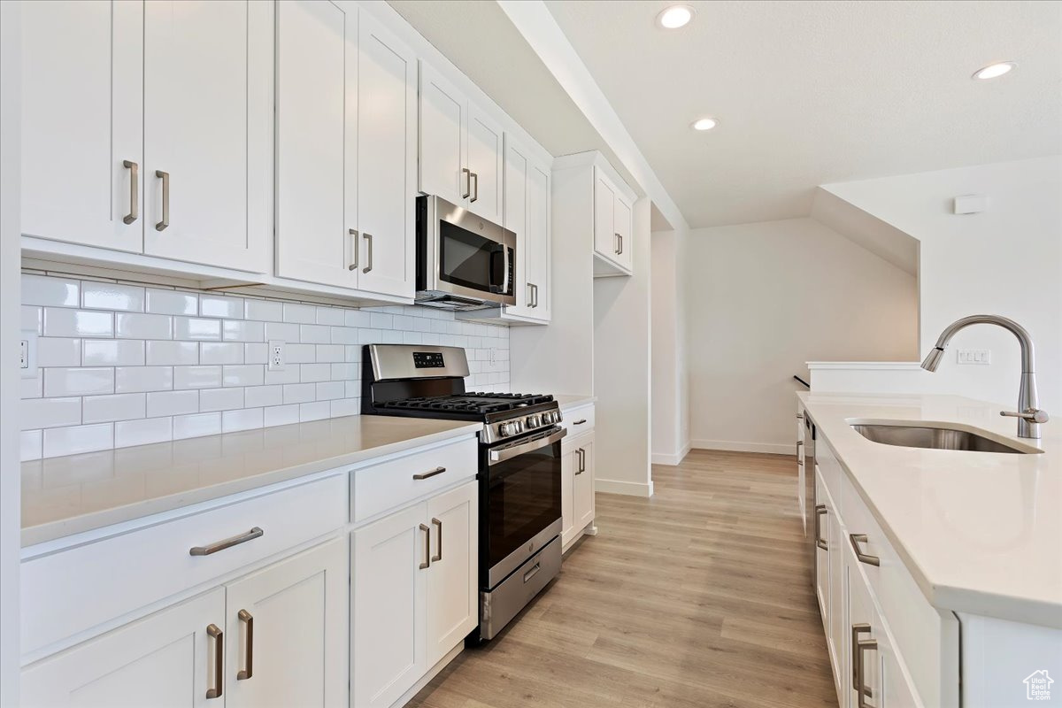 Kitchen featuring white cabinetry, sink, stainless steel appliances, light hardwood / wood-style flooring, and decorative backsplash