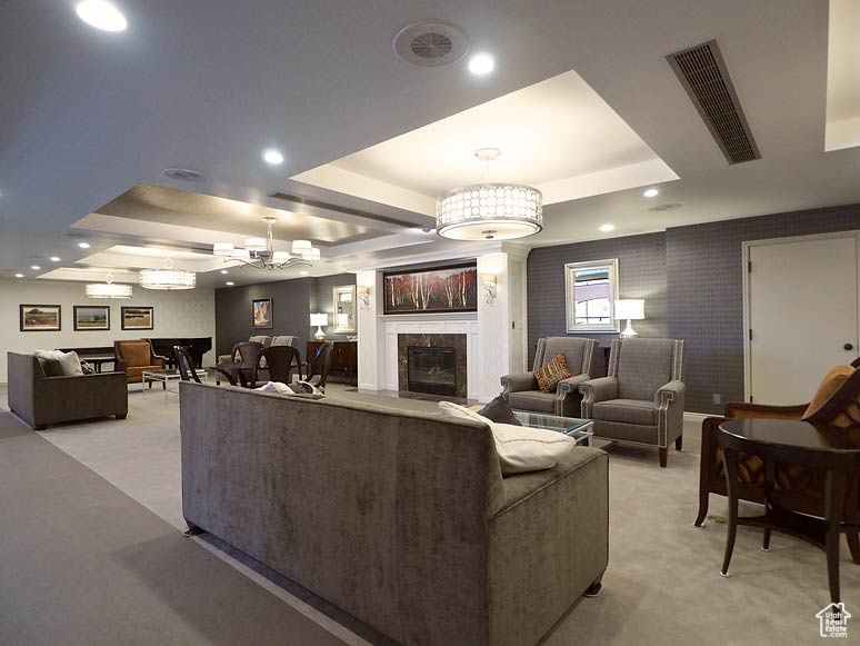 Living room featuring a notable chandelier, a raised ceiling, light carpet, and a tile fireplace