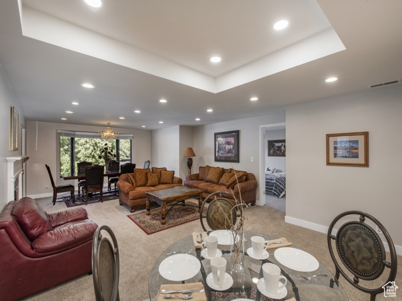 Carpeted living room featuring a tray ceiling and a chandelier