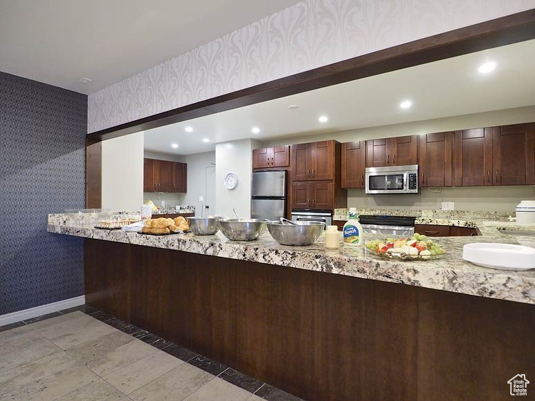 Kitchen featuring kitchen peninsula, appliances with stainless steel finishes, and light stone counters