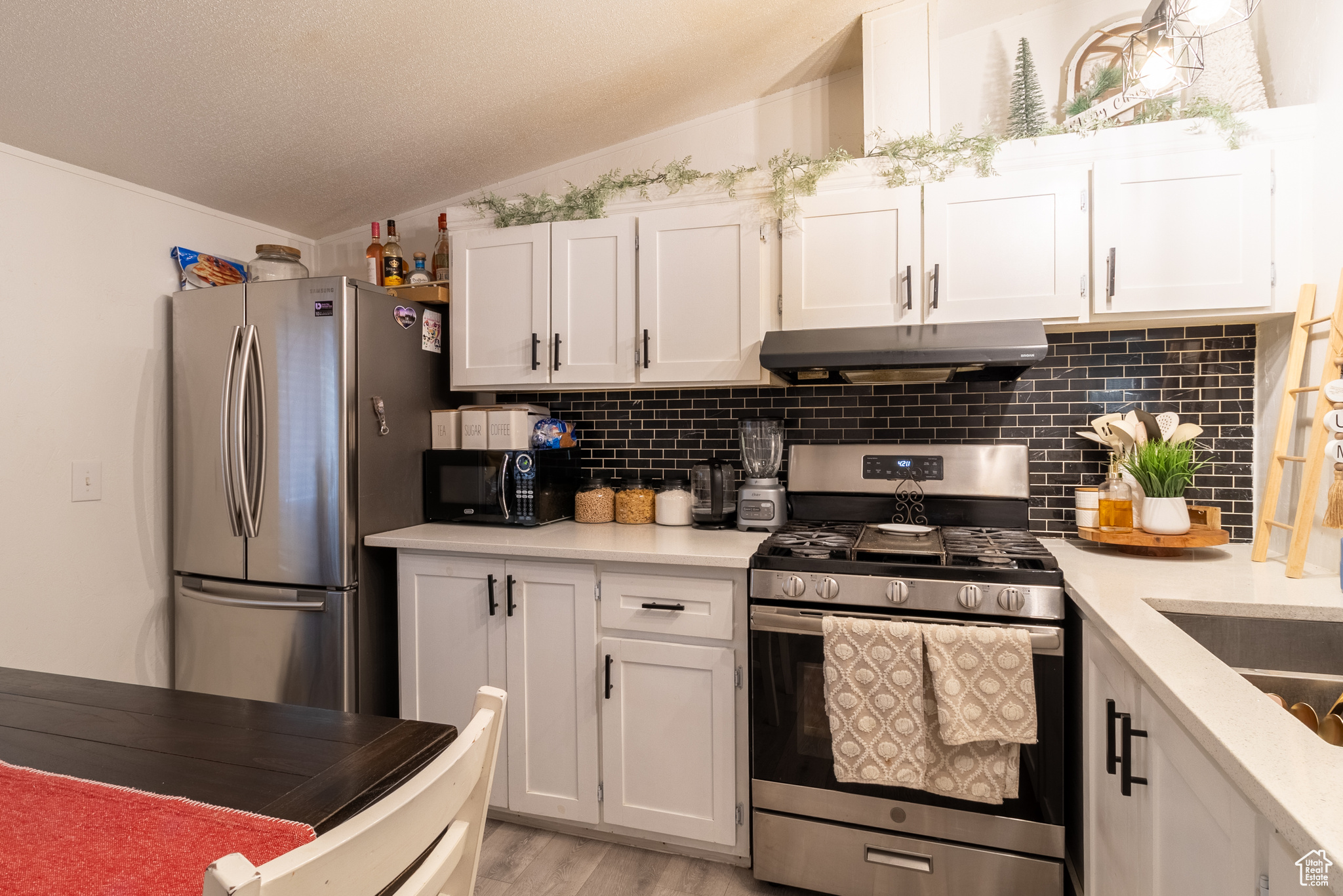 Kitchen featuring lofted ceiling, white cabinets, decorative backsplash, stainless steel appliances, and wood-style floors