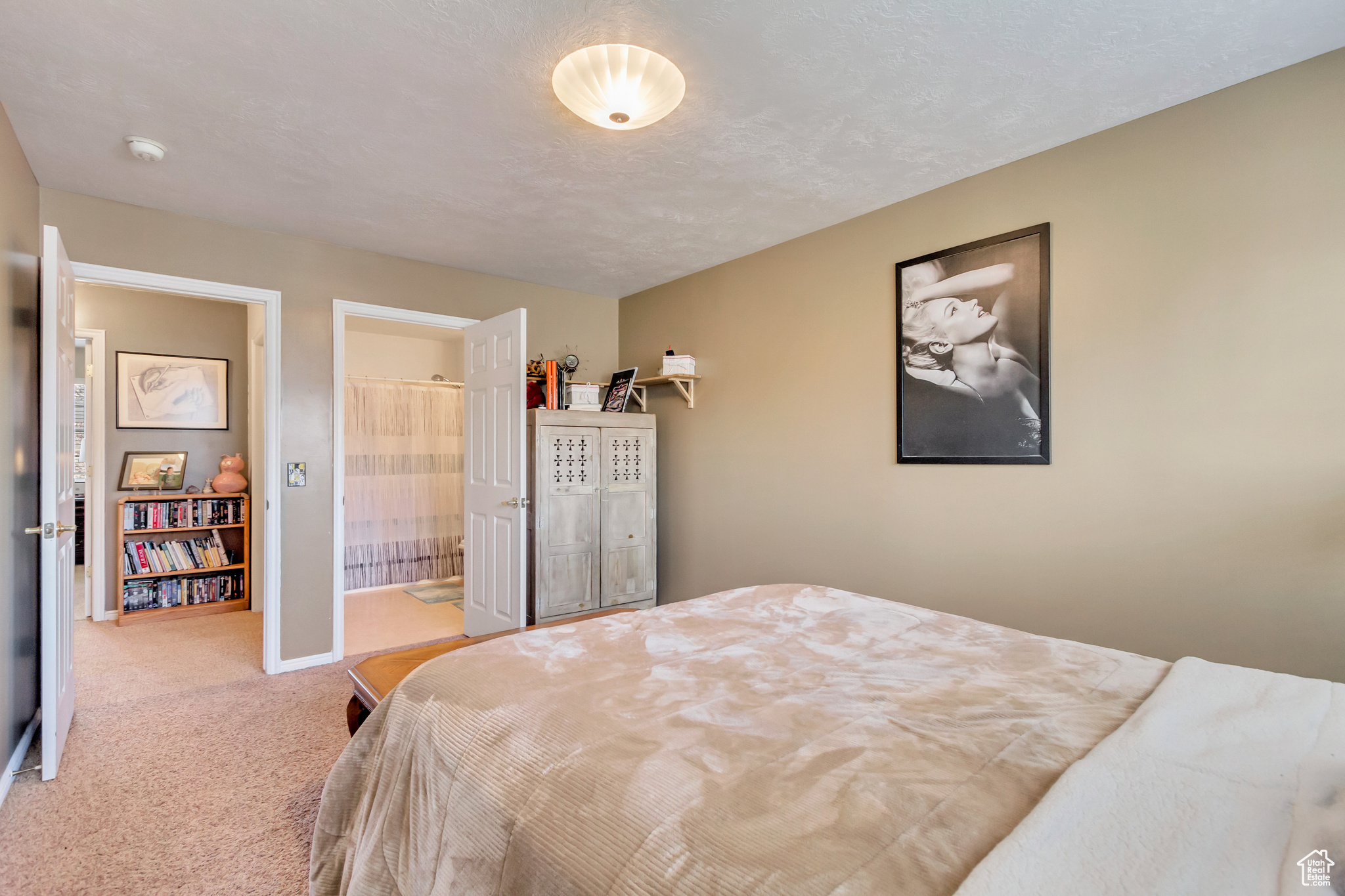 Bedroom featuring ensuite bathroom, light carpet, and a textured ceiling