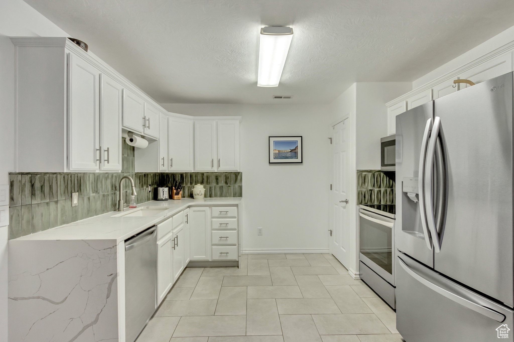 Kitchen featuring backsplash, sink, a textured ceiling, appliances with stainless steel finishes, and white cabinetry