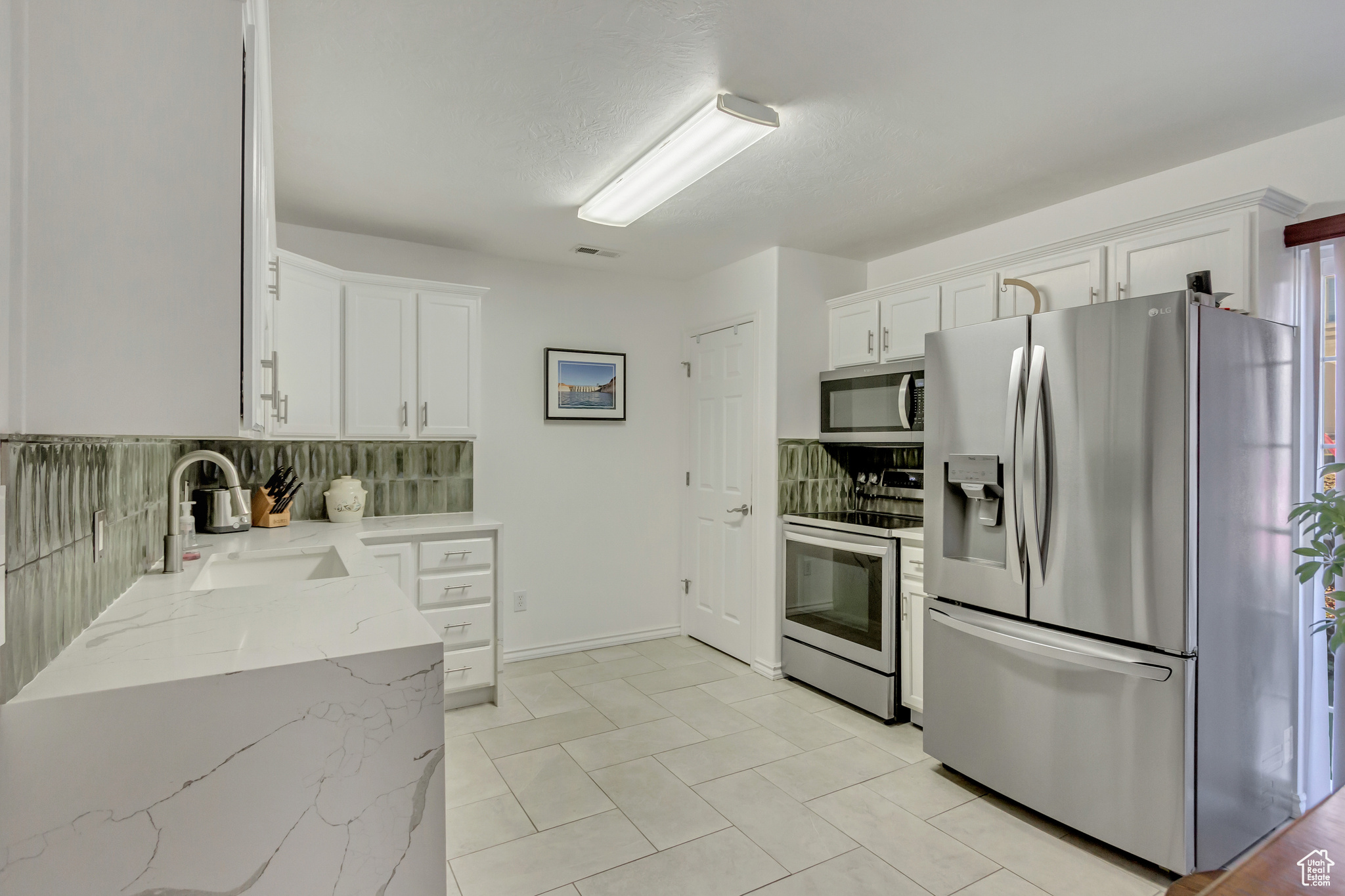 Kitchen with white cabinets, decorative backsplash, light stone counters, and stainless steel appliances