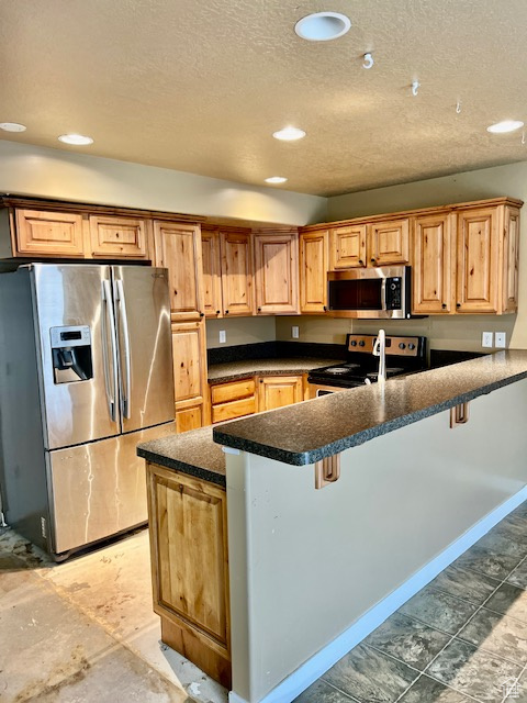 Kitchen featuring a breakfast bar area, kitchen peninsula, stainless steel appliances, and a textured ceiling