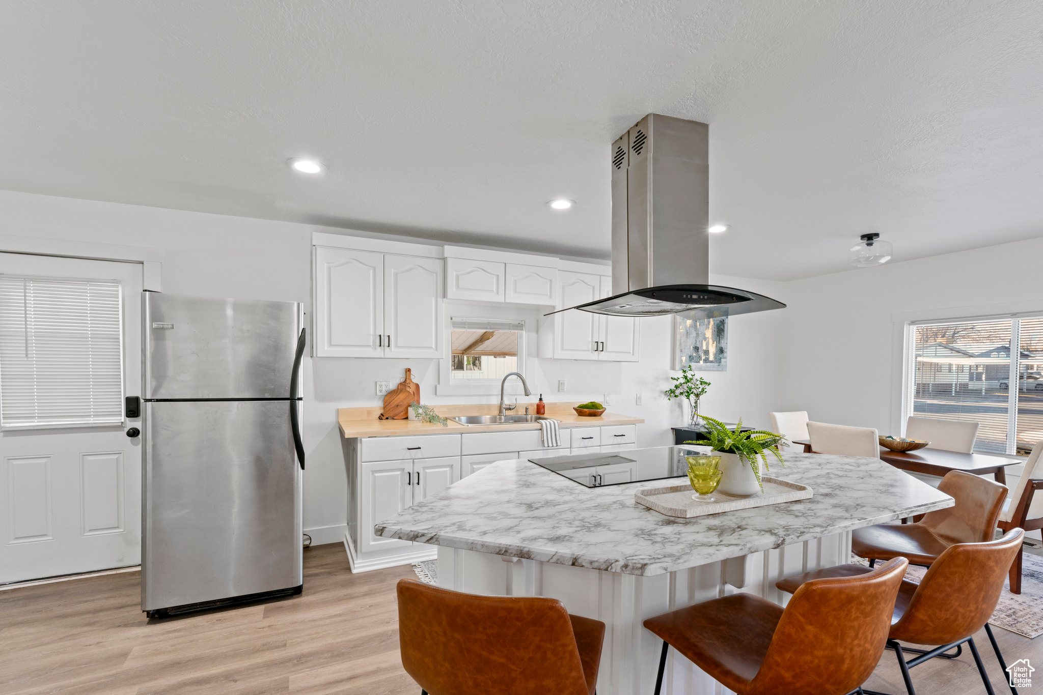 Kitchen with stainless steel refrigerator, sink, island range hood, white cabinets, and light wood-type flooring