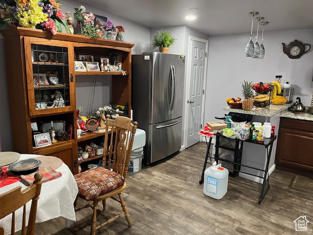 Kitchen with decorative light fixtures, dark hardwood / wood-style floors, stainless steel refrigerator, and light stone counters