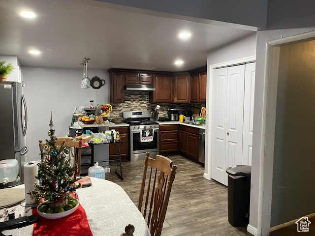 Kitchen featuring dark brown cabinetry, backsplash, stainless steel appliances, and hardwood / wood-style flooring